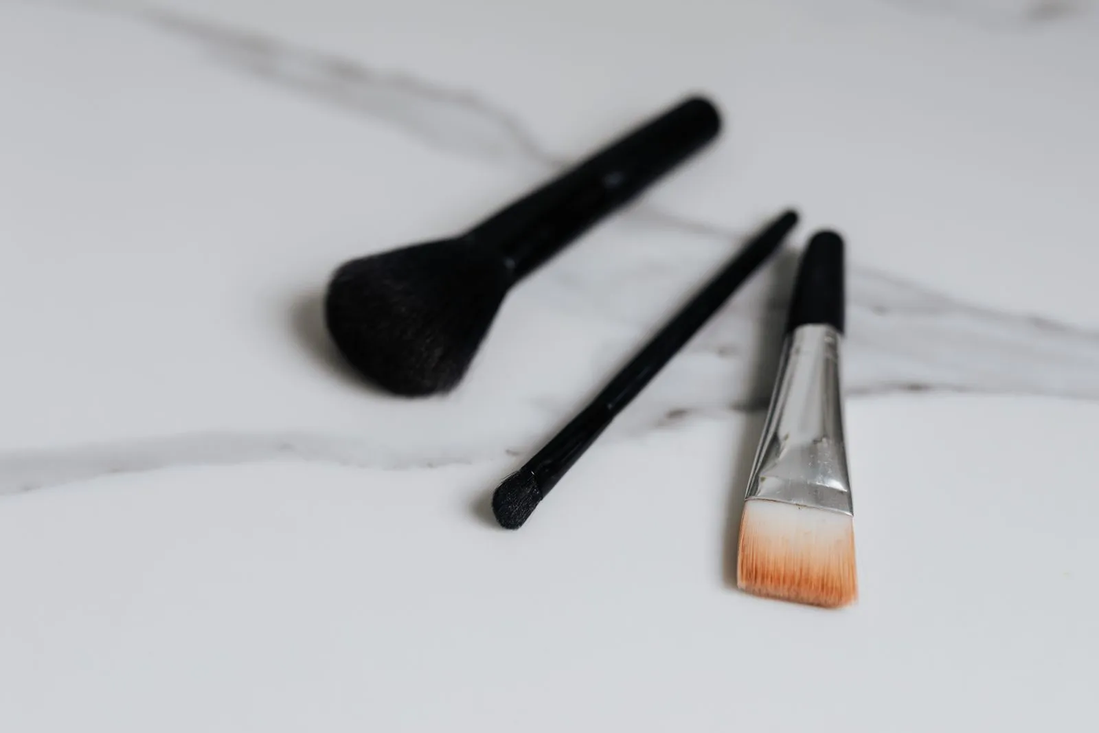 A variety of makeup brushes laid on a clean marble surface