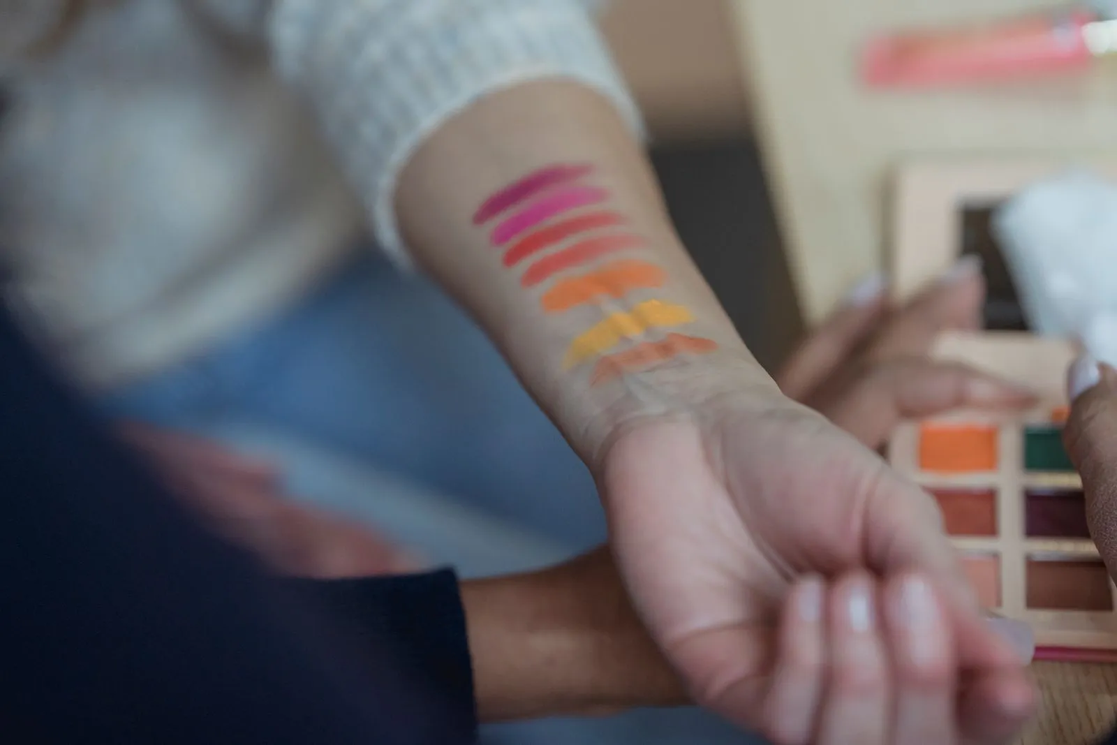 Crop anonymous female makeup artists testing new palette of colorful eyeshadows on arm in modern beauty salon