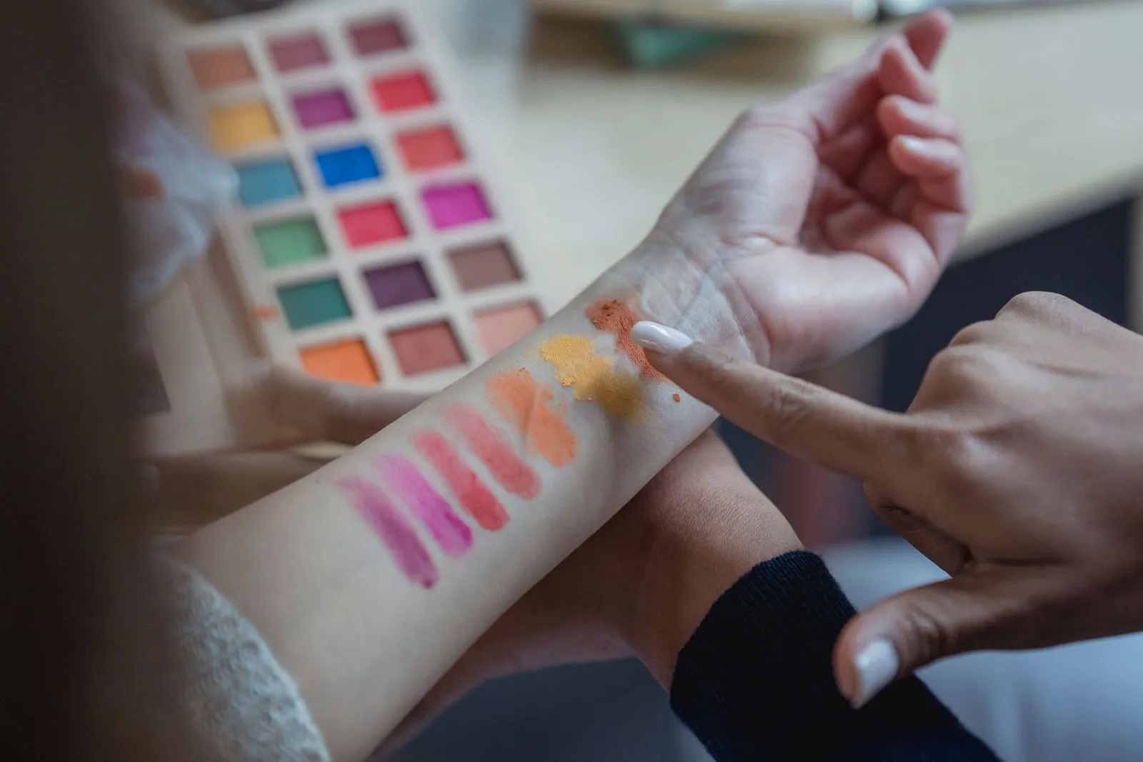 From above of crop unrecognizable young female makeup artist pointing at arm of client while applying colorful eyeshadow