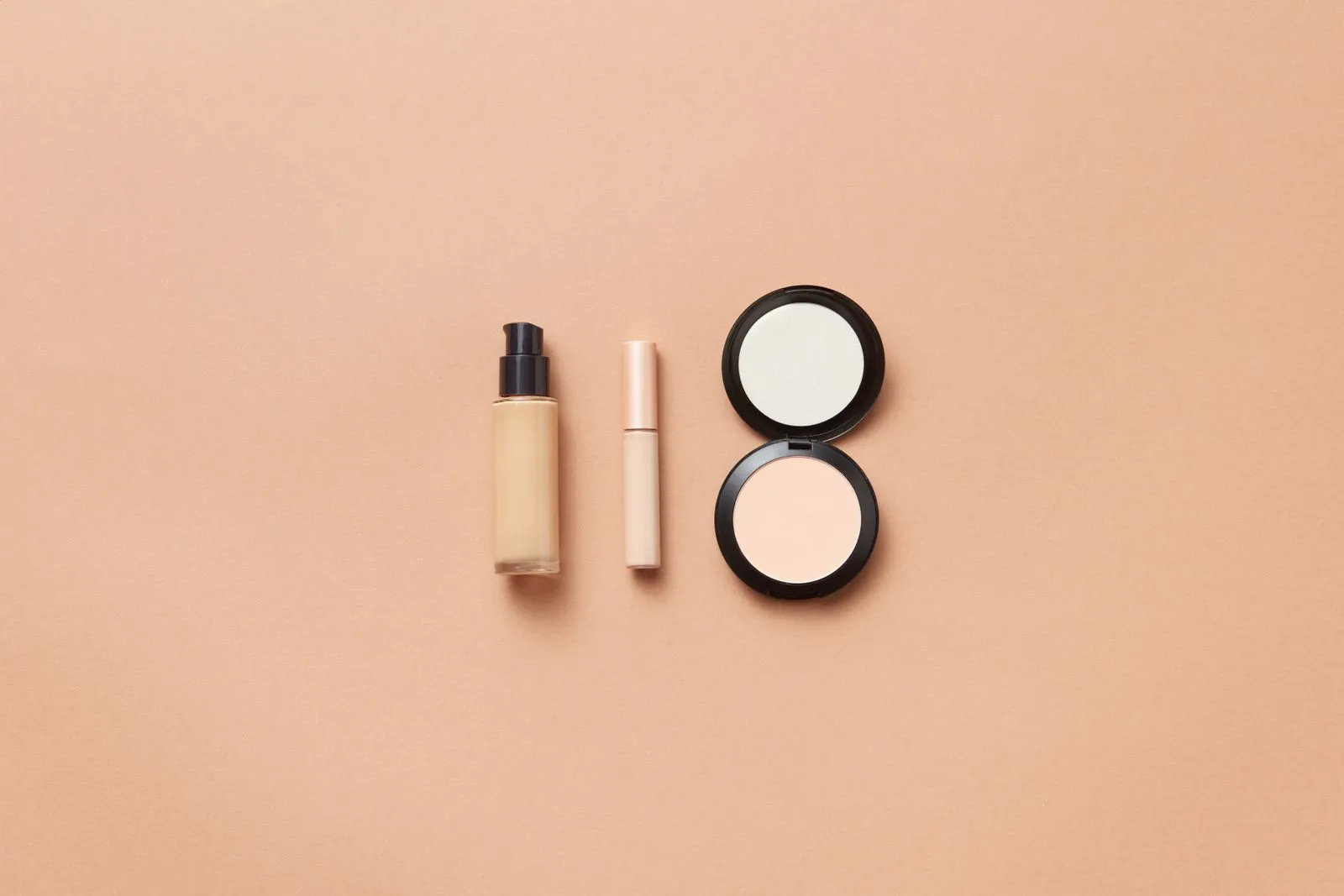 Flatlay of foundation, concealer, and compact powder on beige background