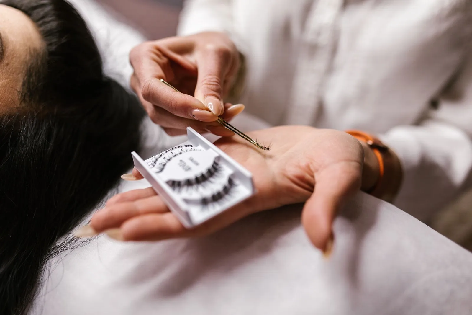 Close-up of an eyelash extension application using tweezers, featuring a beautician's hands.