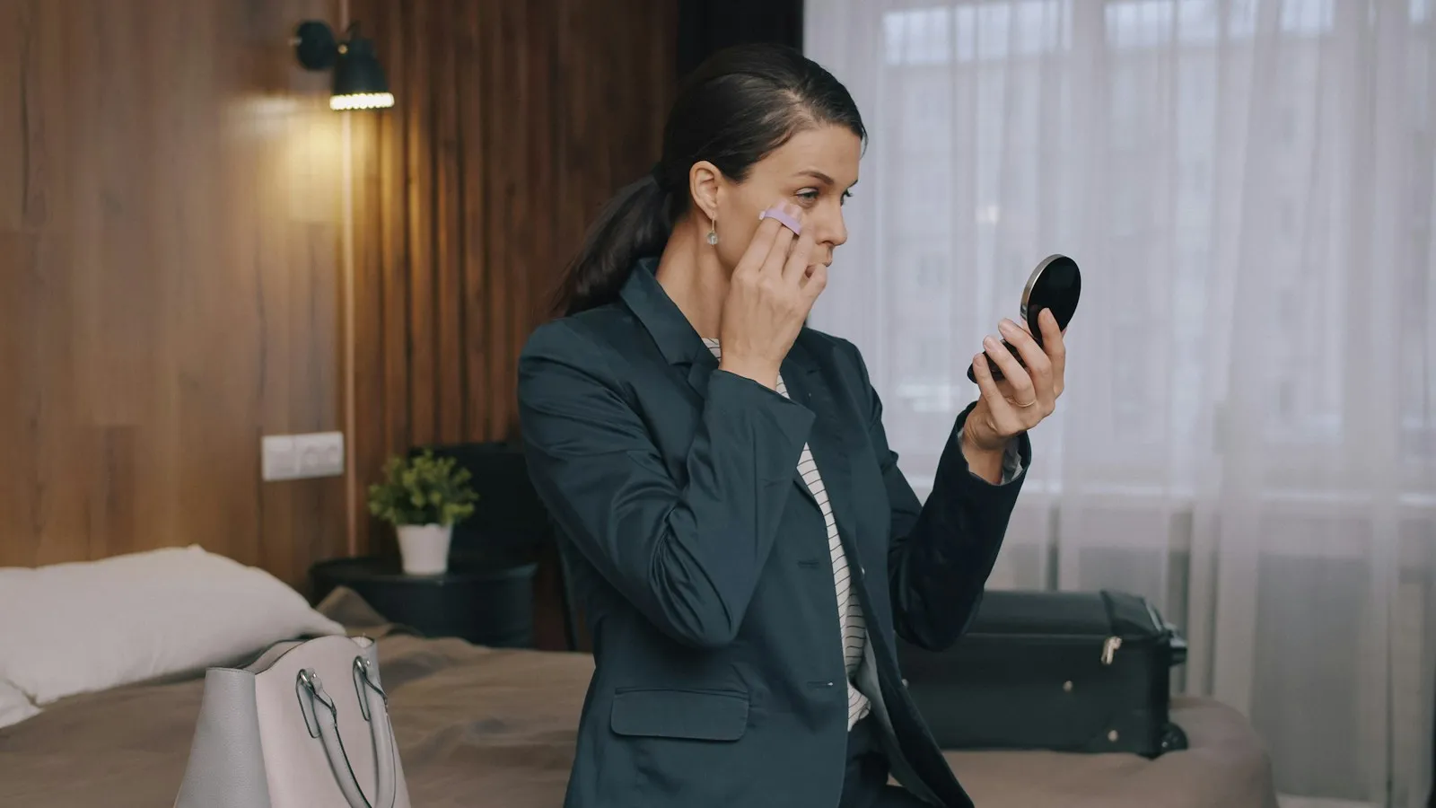 Slow motion of young businesswoman in suit putting on make-up in hotel room using face powder. Beauty, travelling and li