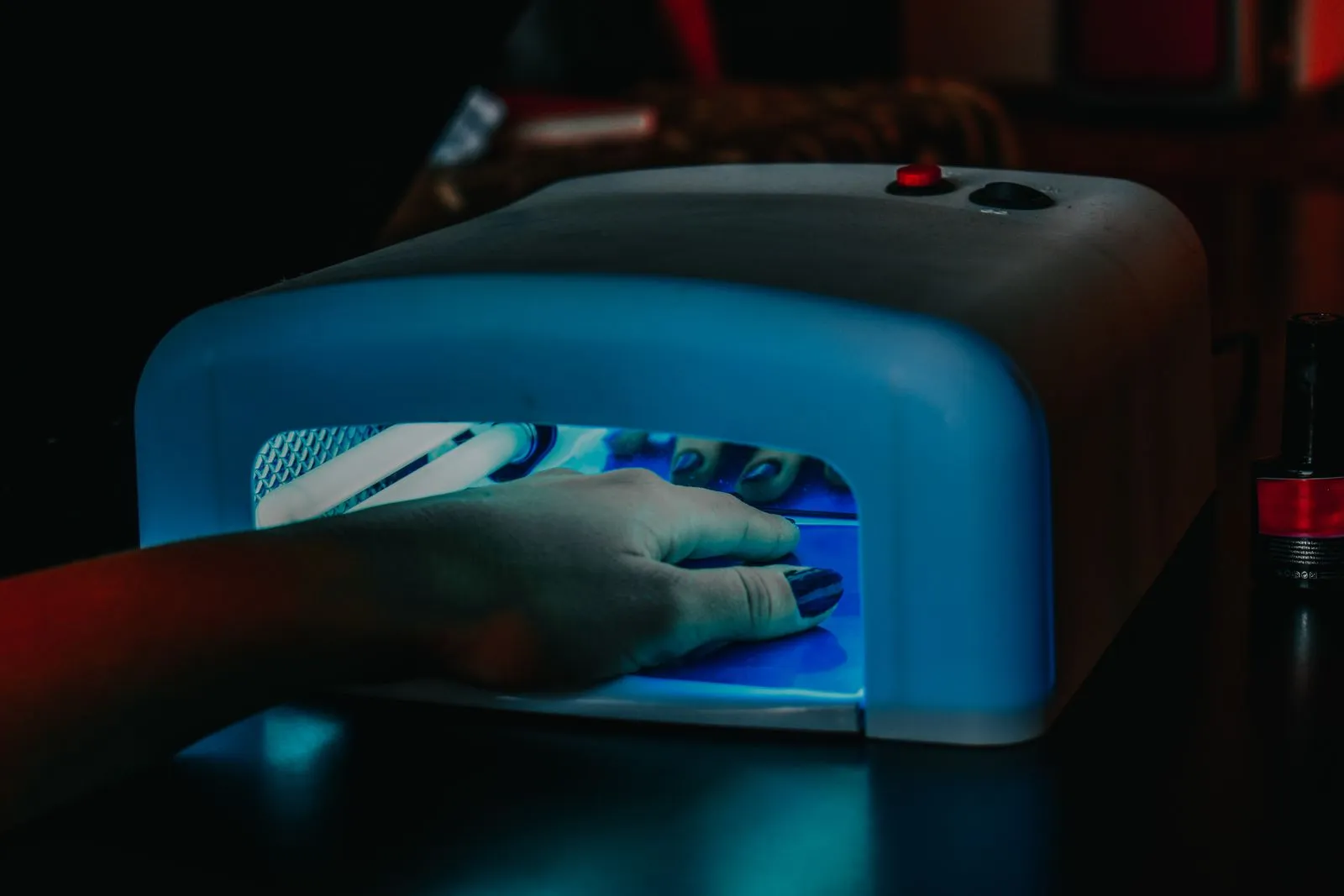 A hand with manicured nails being cured under a blue LED lamp for gel polish.