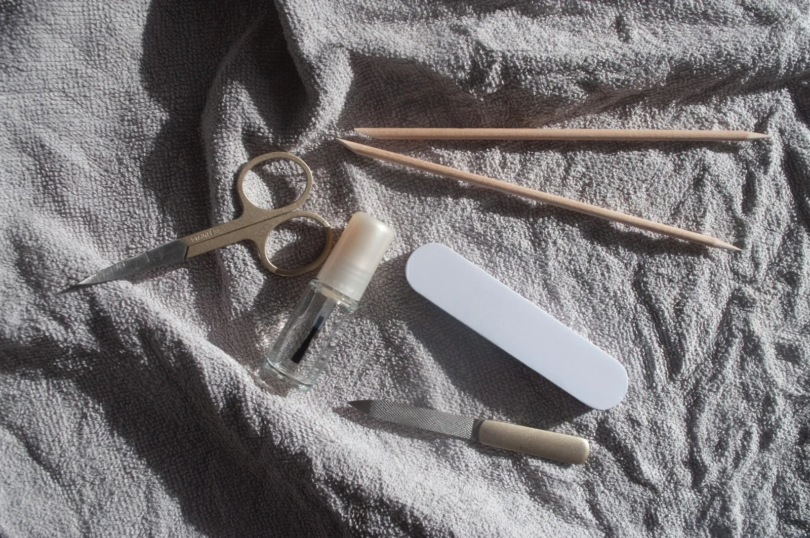 Top view set of manicure equipment on a gray towel background on a sunny day. Pedicure kit. Transparent strengthening na
