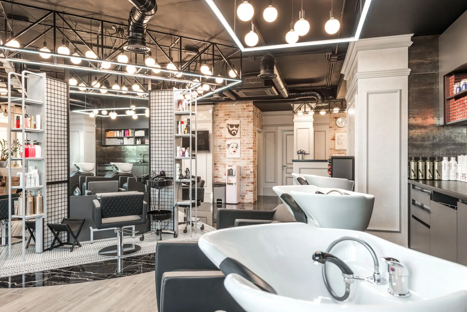 Backwash chairs with sinks placed in stylish spacious beauty salon with mirror and various cosmetology products under br