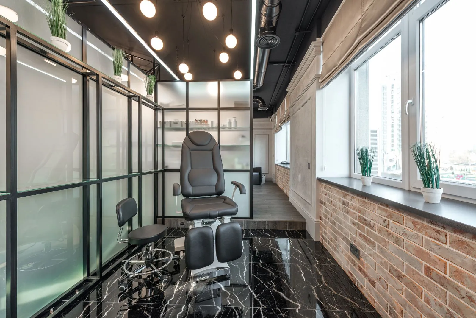 Black leather pedicure chair placed between glass door and window in modern beauty salon with decorated plants and glowi