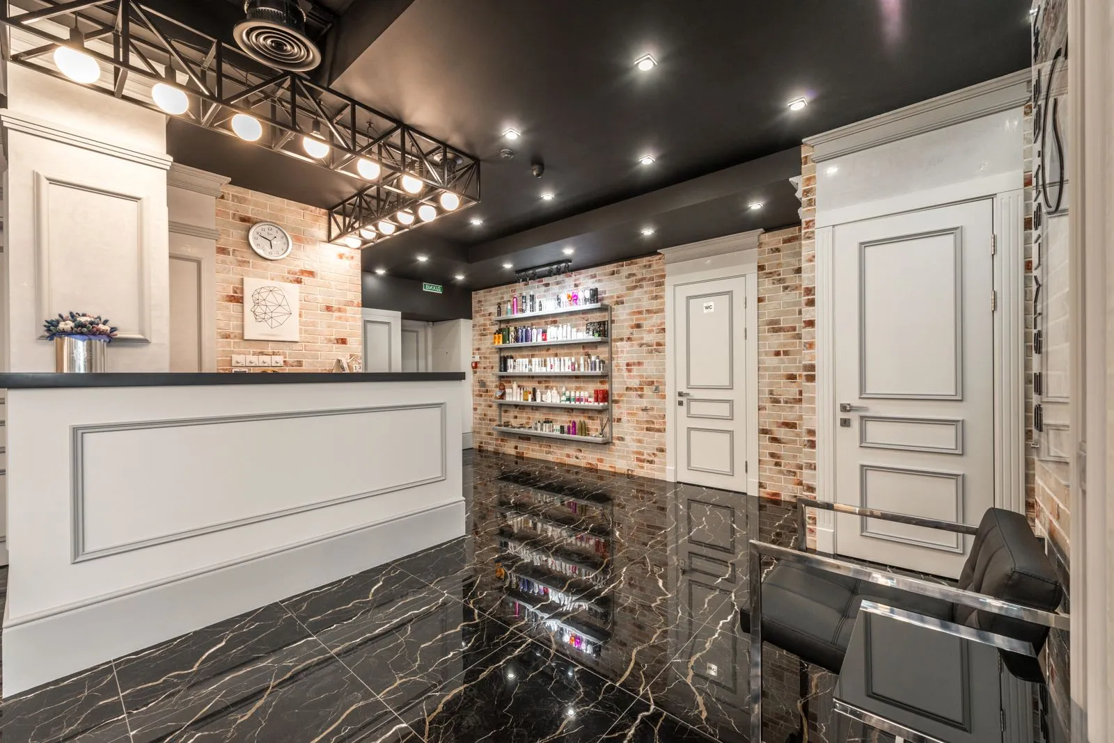 White reception counter with flowers placed in stylish beauty salon with doors and shelves with various cosmetology supp