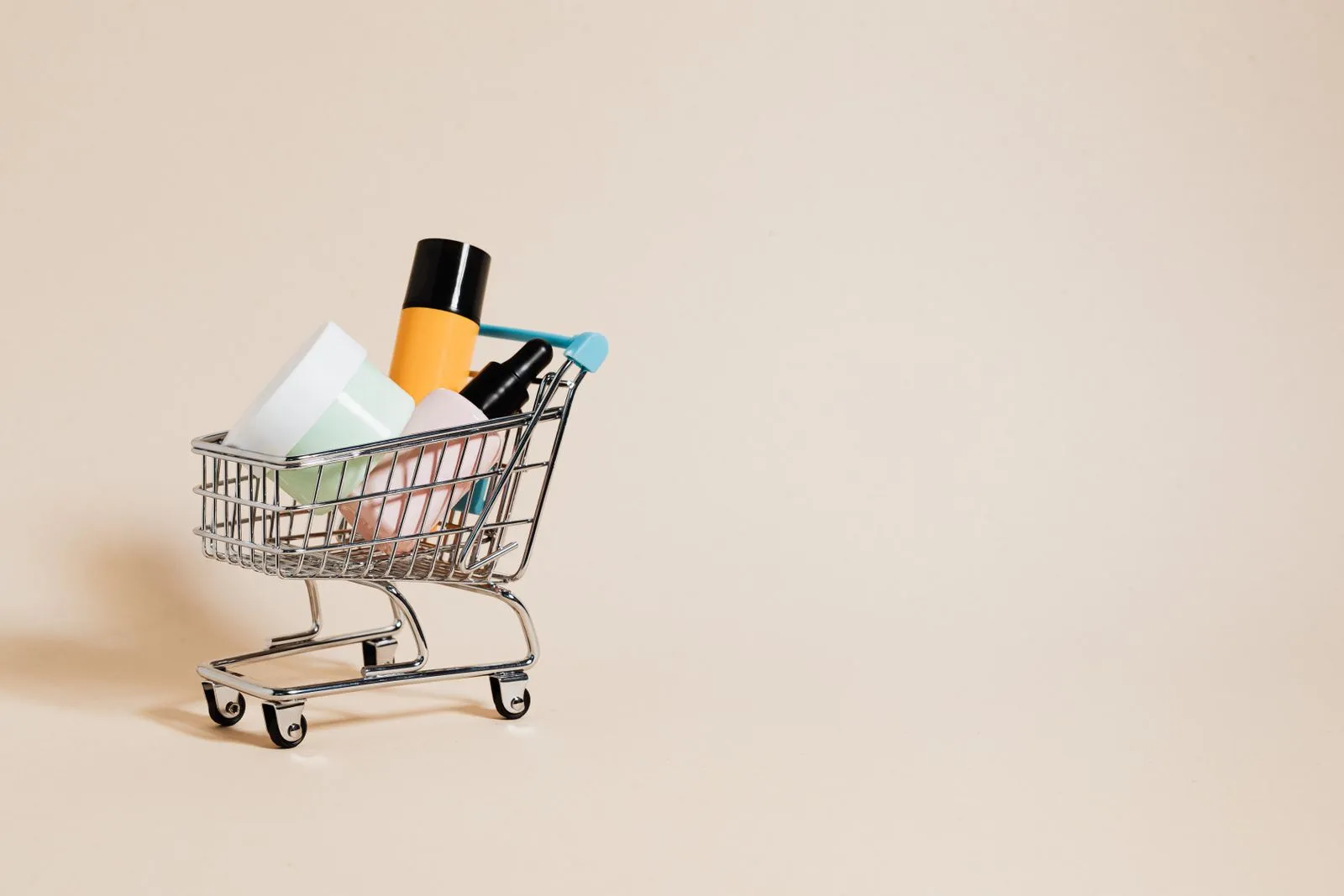 A minimalist image of a mini shopping cart filled with cosmetics on a beige background