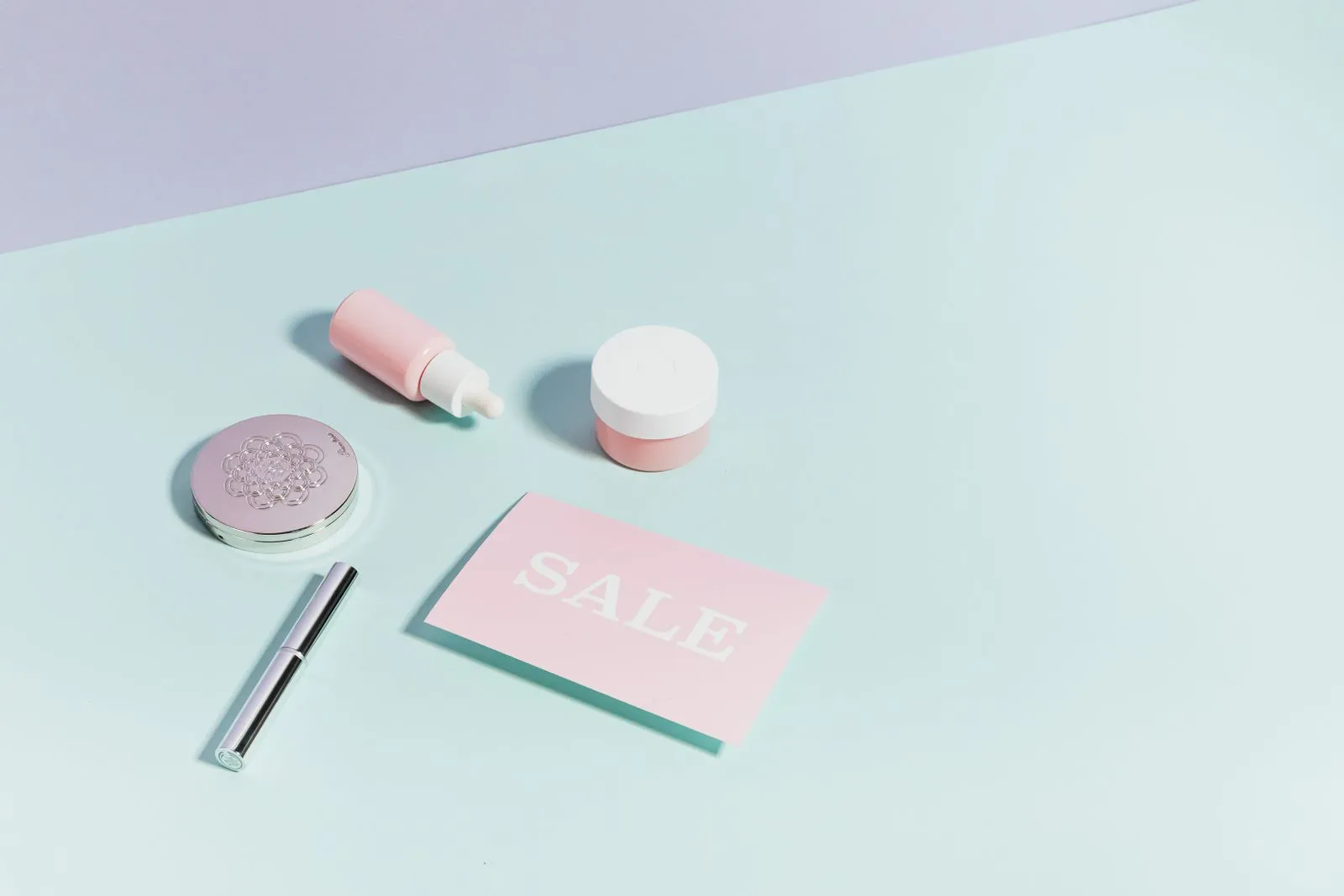 Clean flat lay of pastel pink beauty products and sale card on a light background.