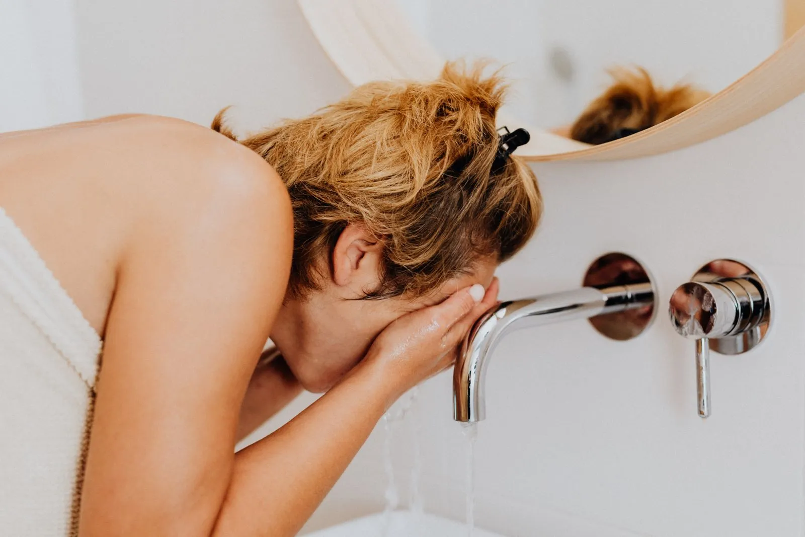 Adult woman washing her face at a modern bathroom sink during the morning routine.
