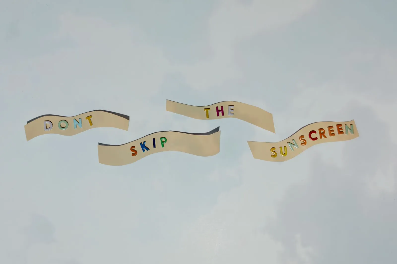 Colorful cutout letters forming a reminder to wear sunscreen against blue sky.