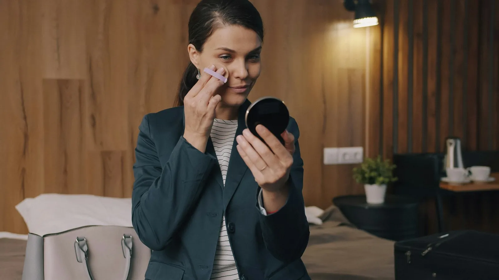 Attractive young woman is putting on make-up smiling in mirror then leaving hotel room, girl is using compact face powde