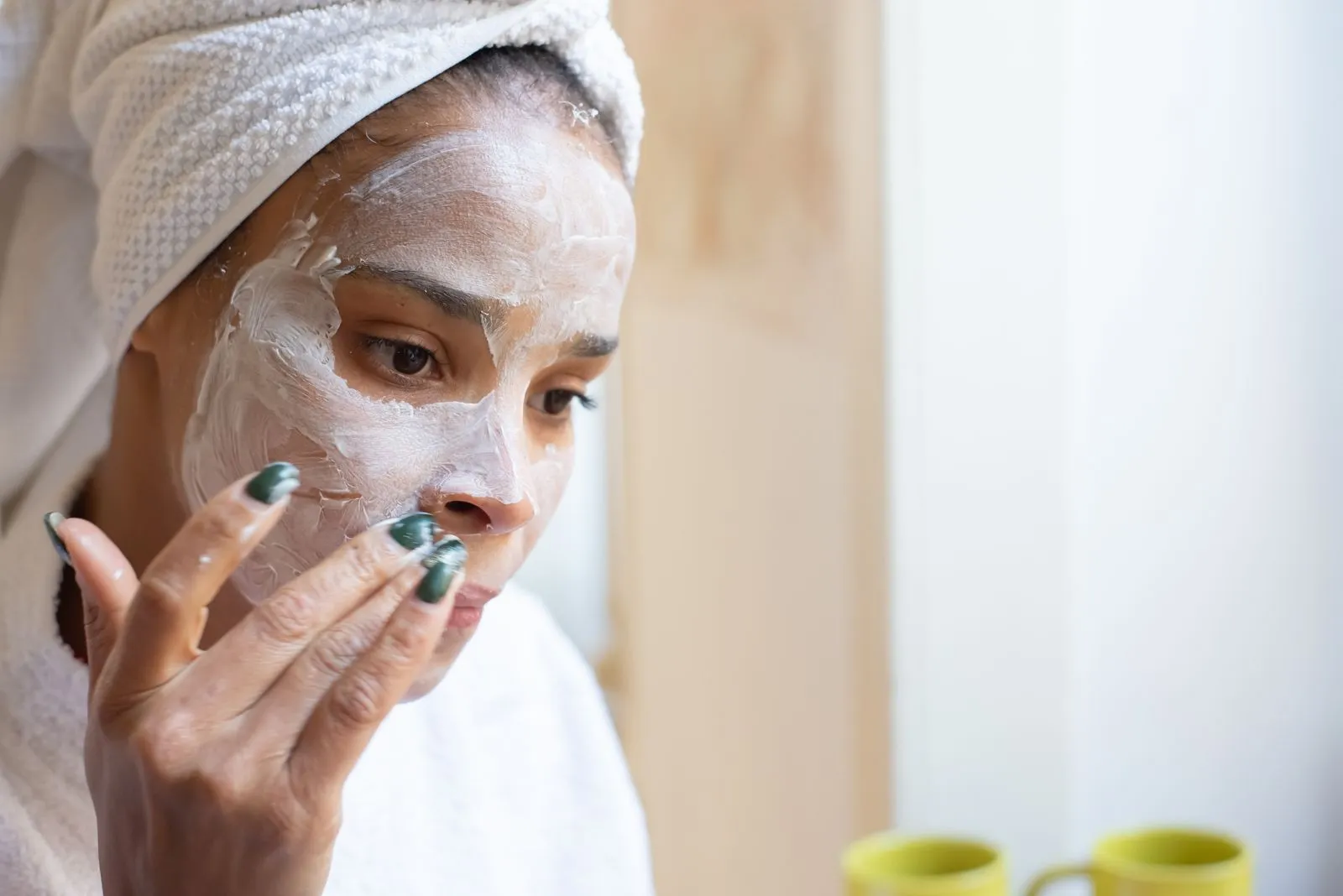 A woman applies moisturizing cream on her face during a home spa routine, enhancing her skincare regimen.