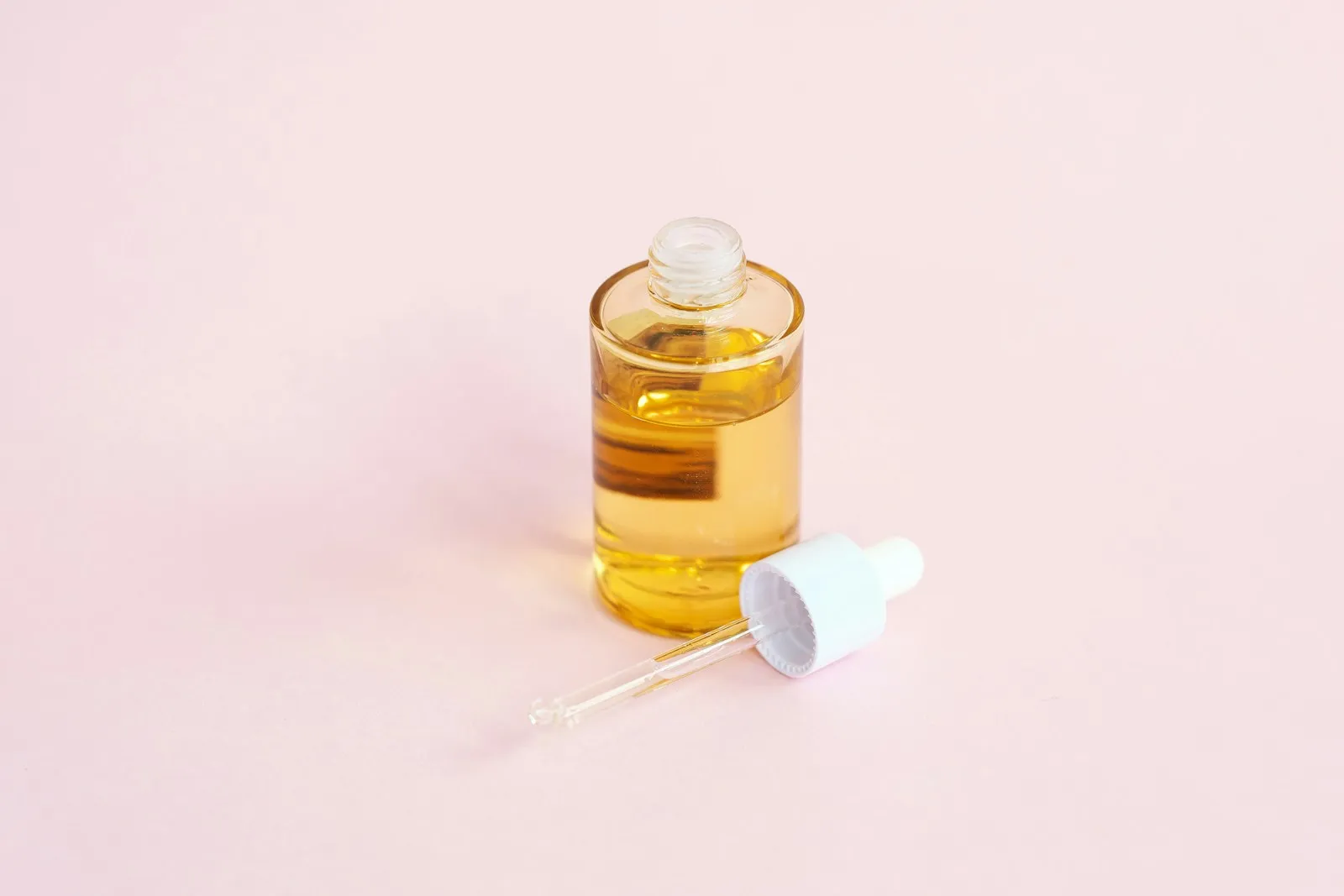 Skincare serum bottle and dropper on a pink surface