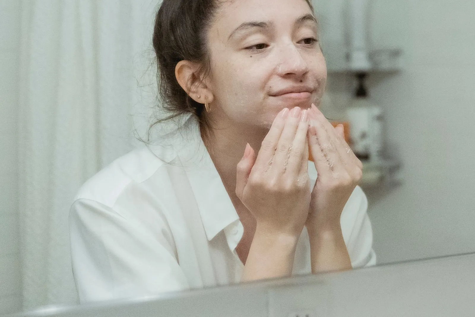 A woman applies facial cream, enjoying her skincare routine in front of a bathroom mirror.