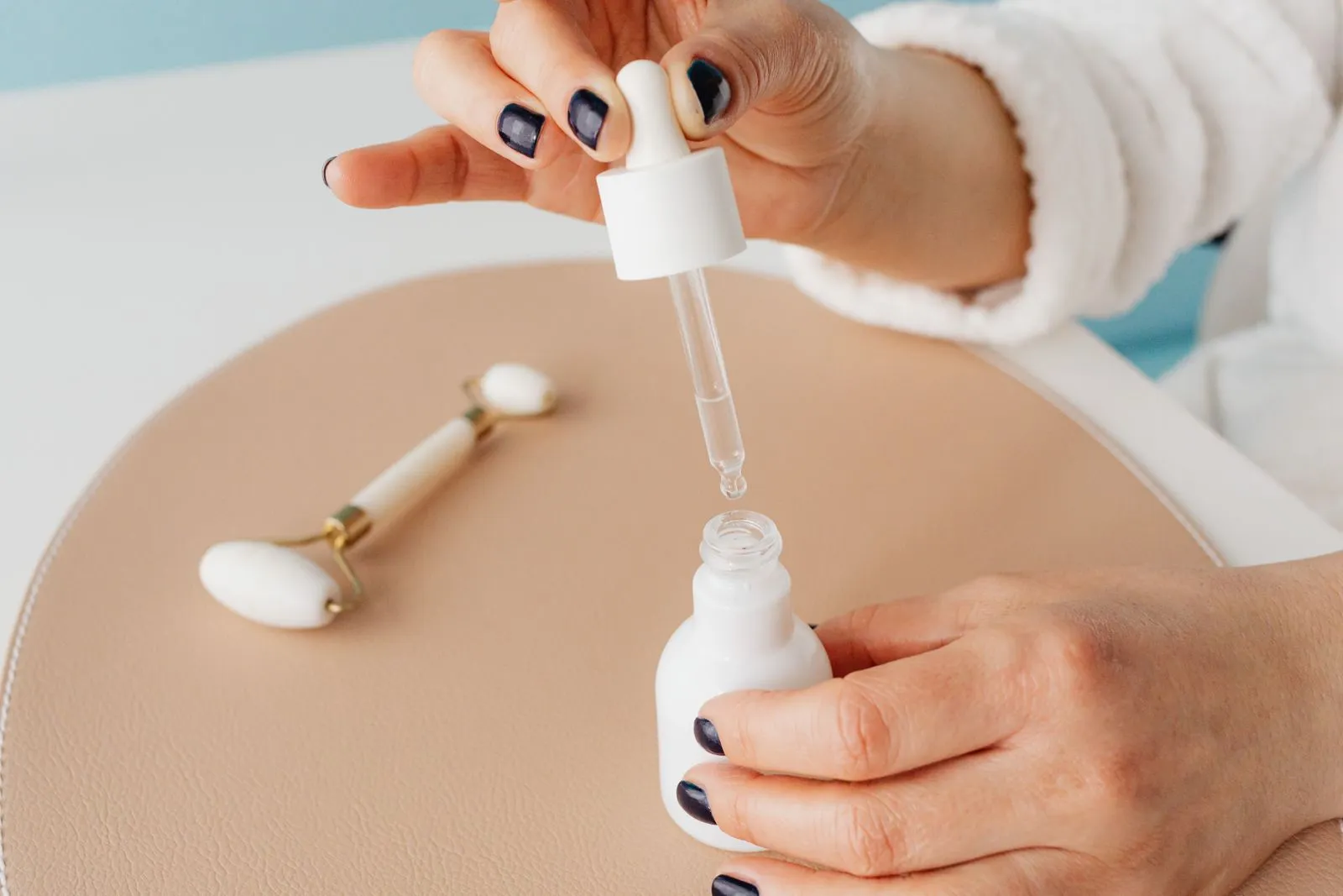 Close-up of hands using serum dropper with jade roller