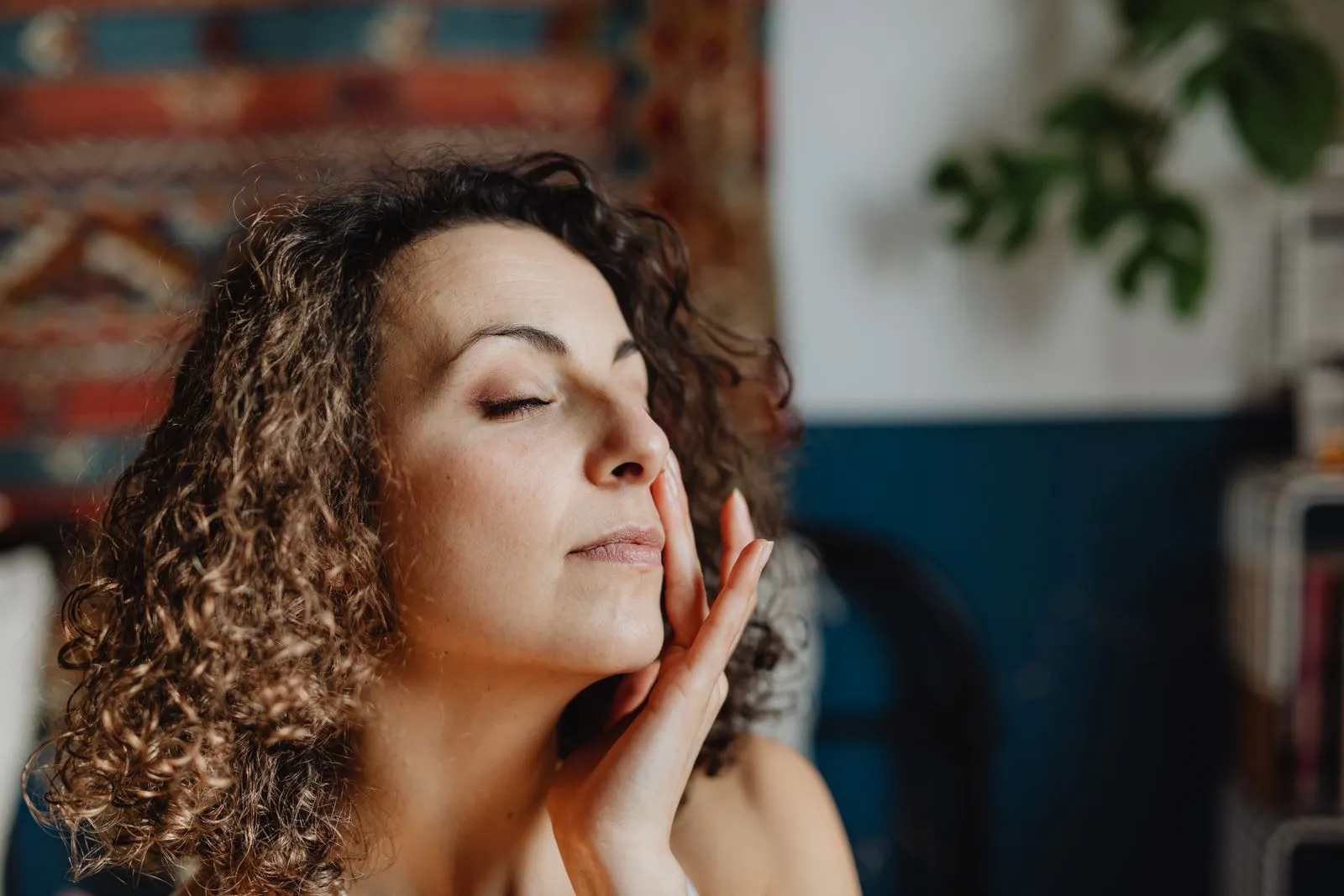 A relaxed woman with curly hair enjoying a skincare routine indoors.