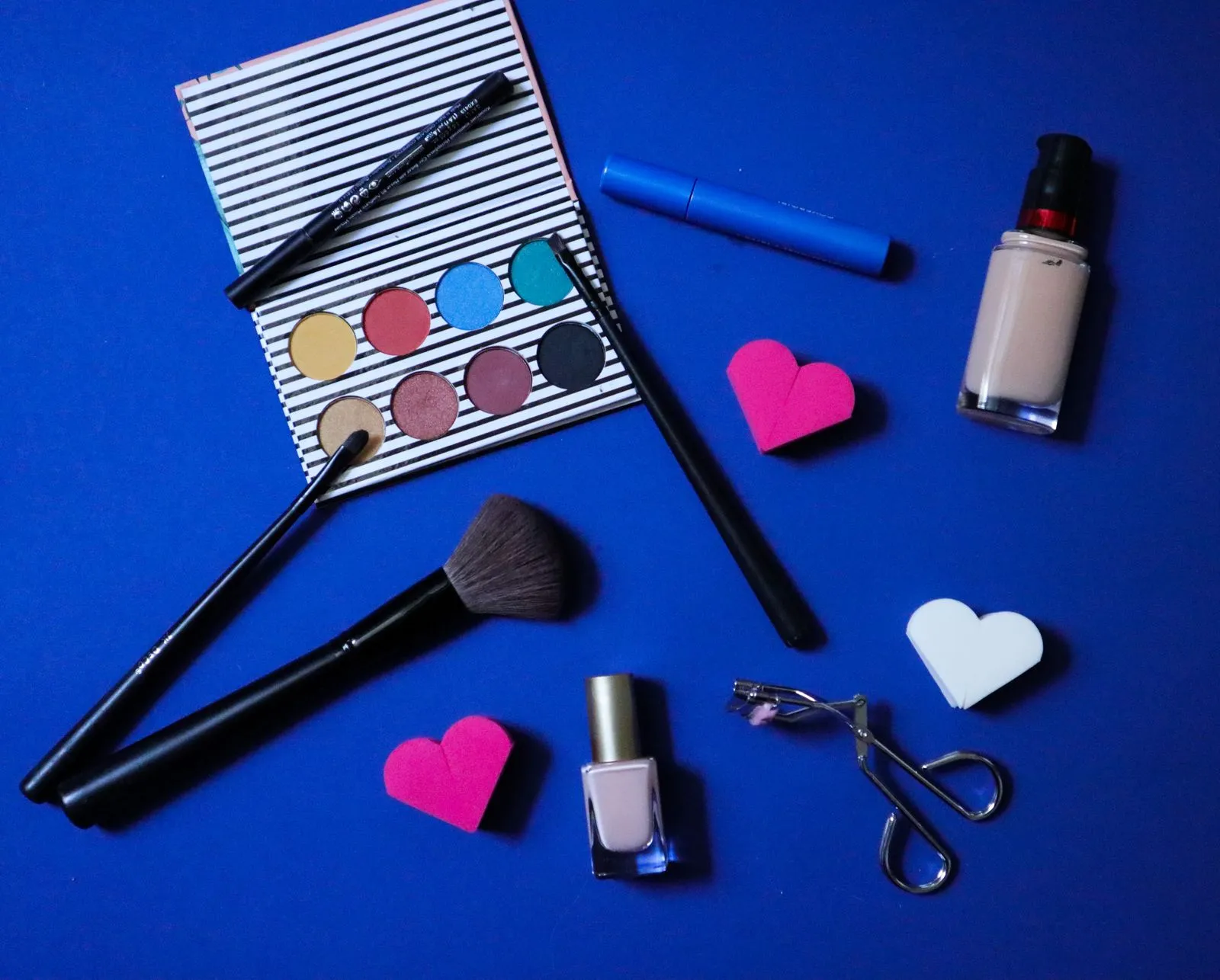 Colorful makeup products arranged stylishly on a blue backdrop for beauty inspiration.