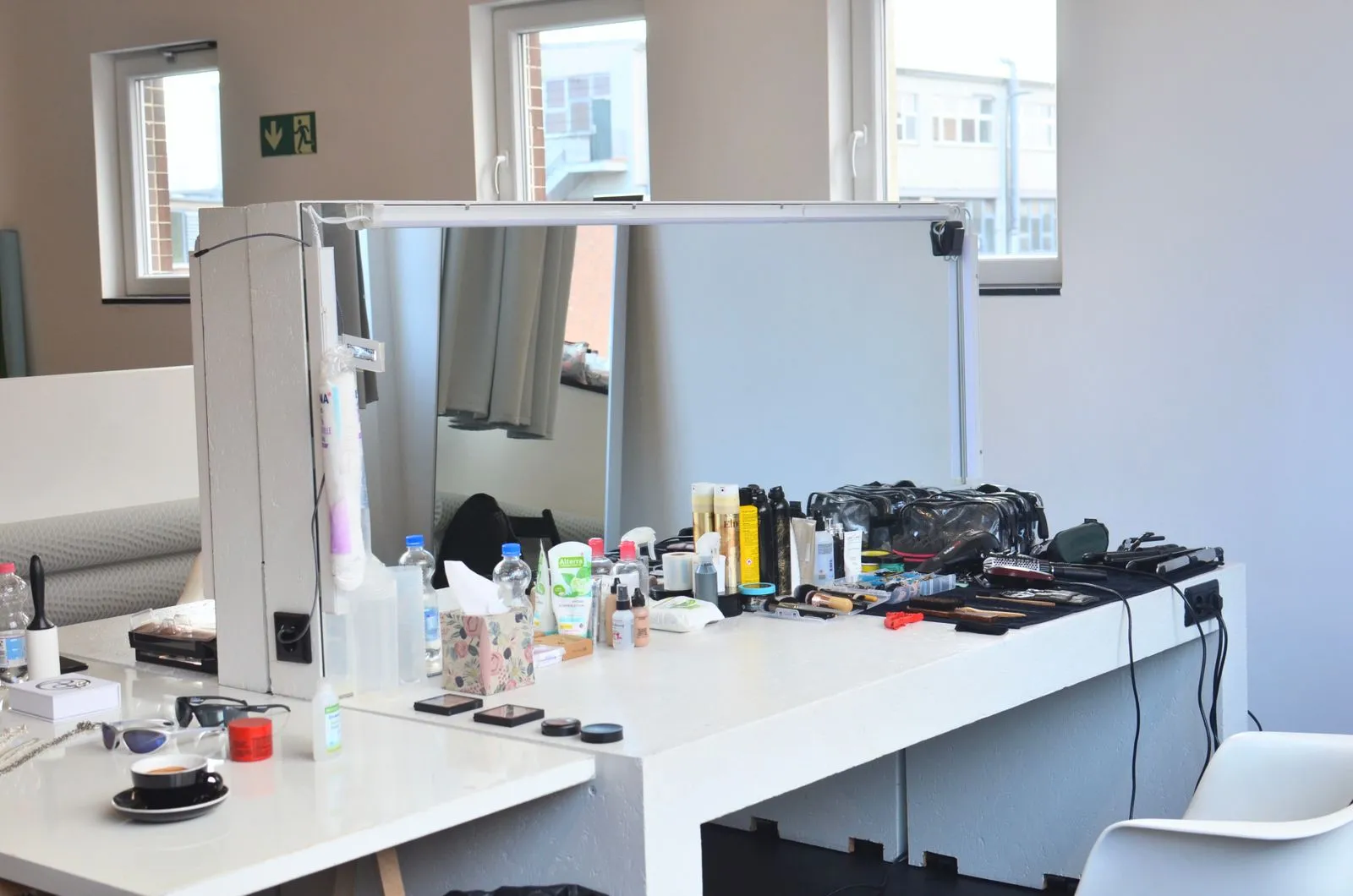 White dressing table with cosmetic products and instruments near table with coffee placed in light room with windows and