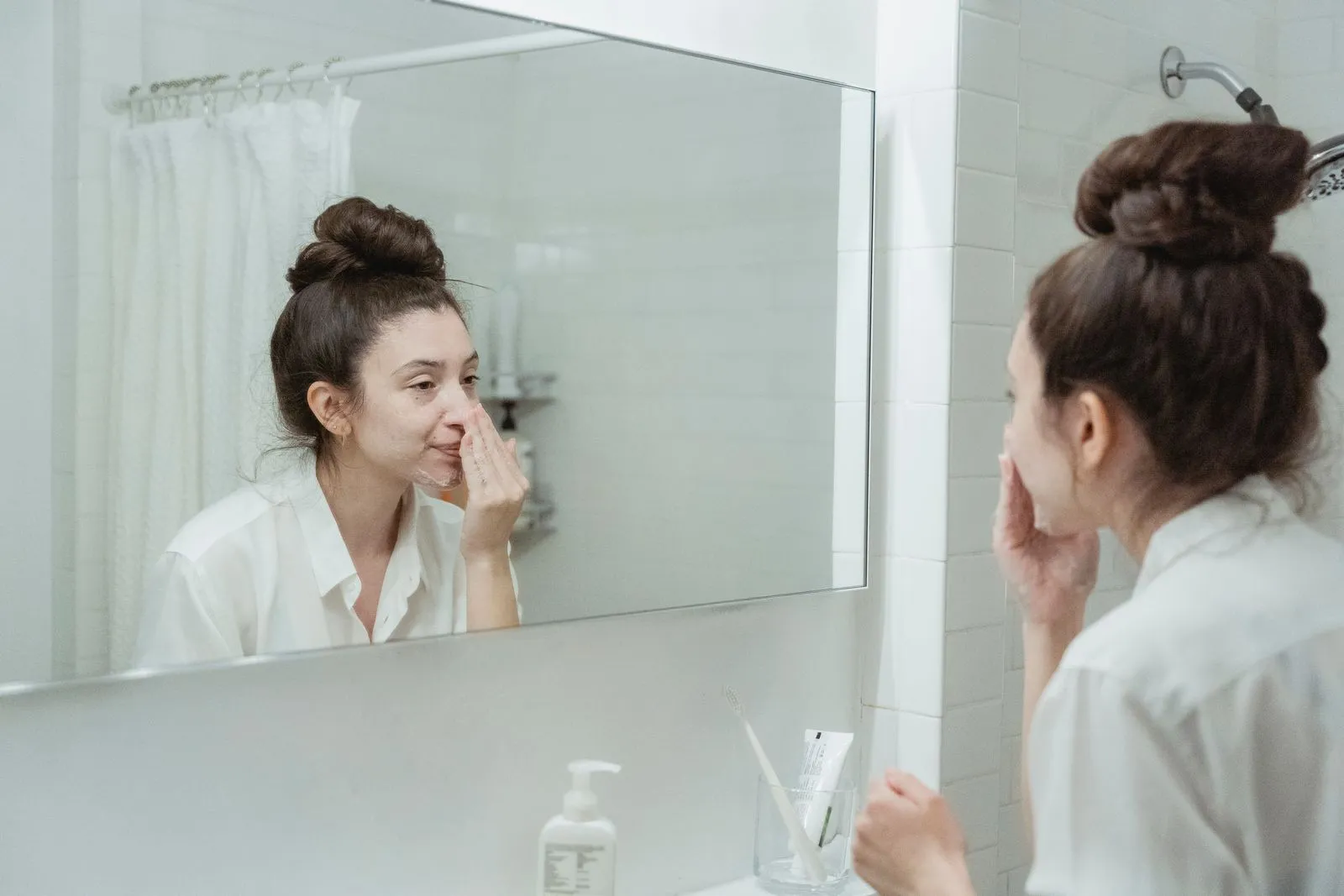 Caucasian woman in bathroom applying skincare product while looking in the mirror.