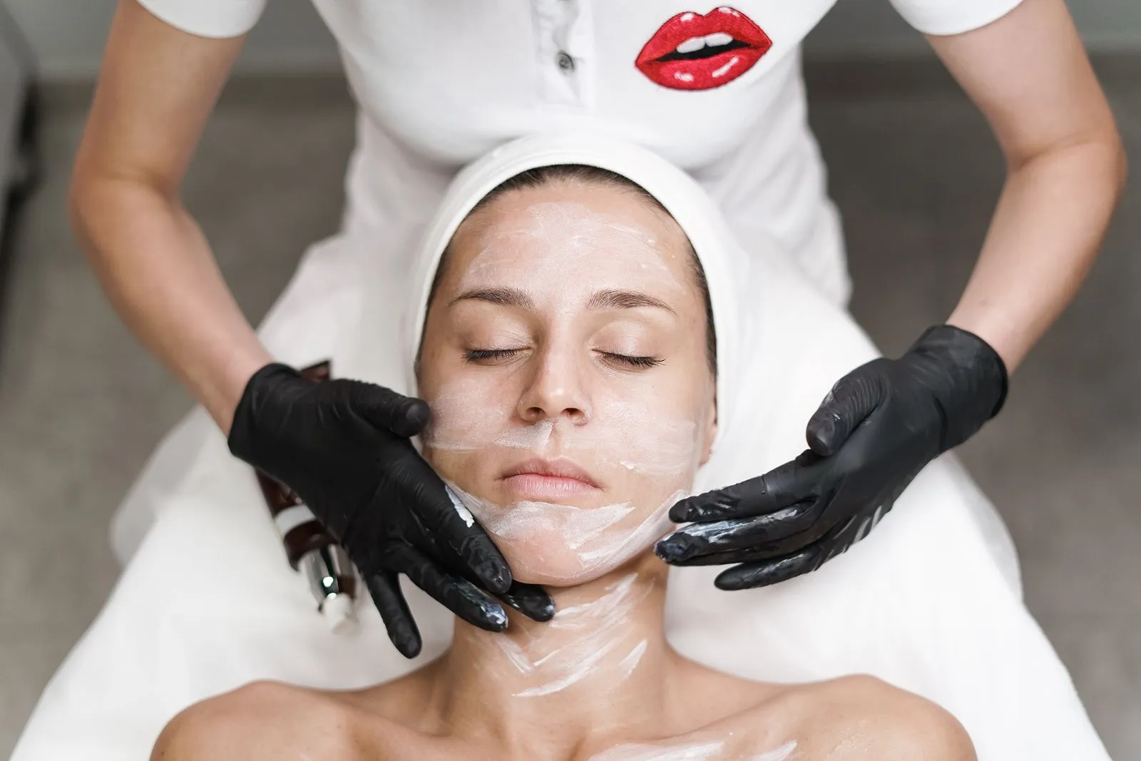 Woman receiving a facial treatment at spa, with beautician applying mask in a relaxing setting.