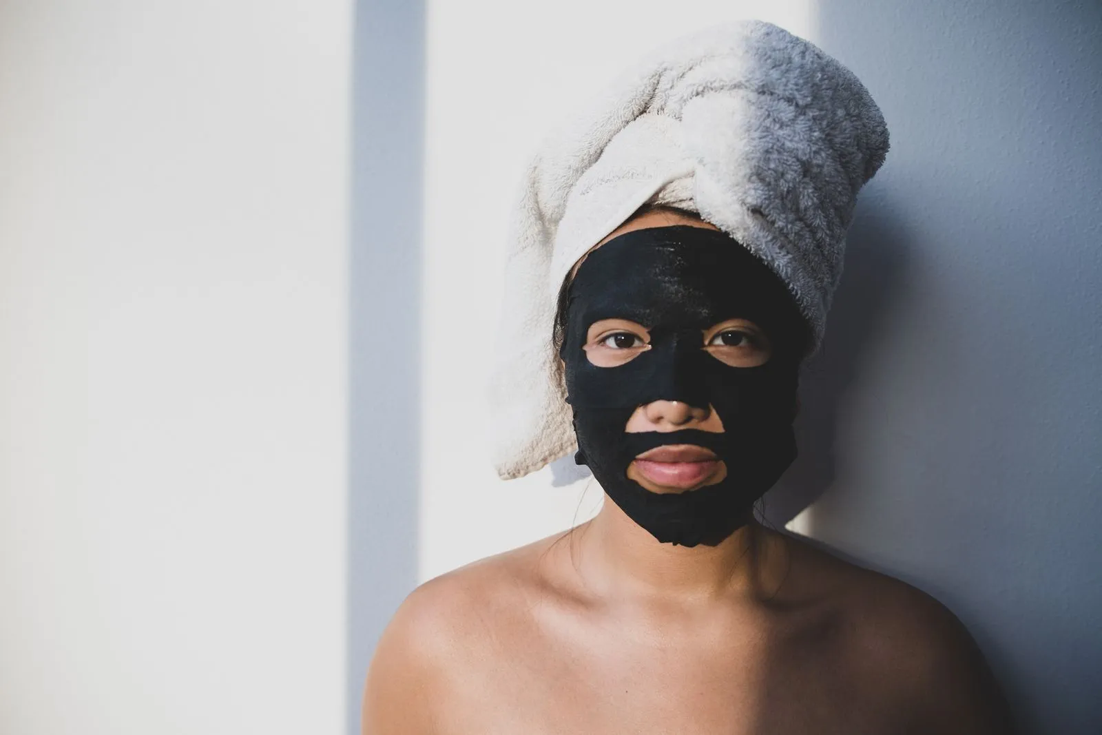 A woman with a towel wrapped around her head wearing a black facial mask