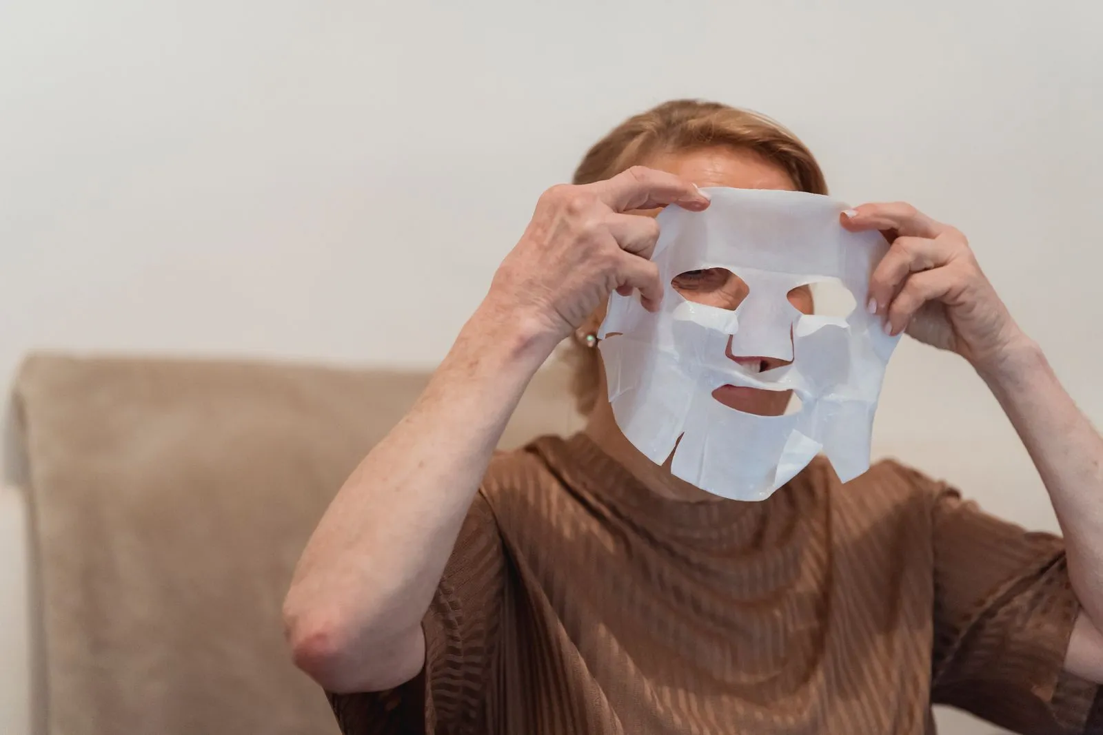 Senior woman applying a sheet face mask for skincare and relaxation indoors.