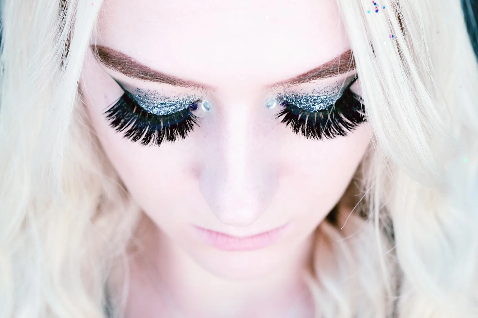 A close up portrait looking down on an 18 year old person wearing false eyelashes and glitter eye shadow.