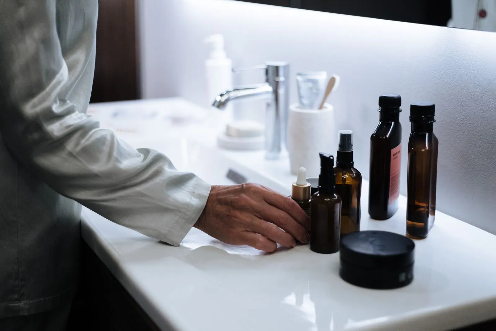 A hand reaching for skincare products on a modern bathroom sink.