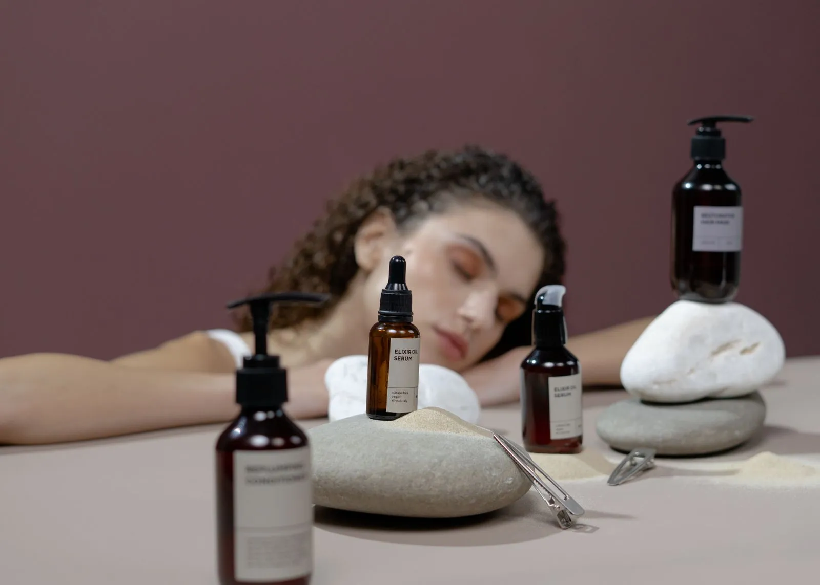 Woman with curly hair surrounded by natural stones and haircare products, eyes closed.