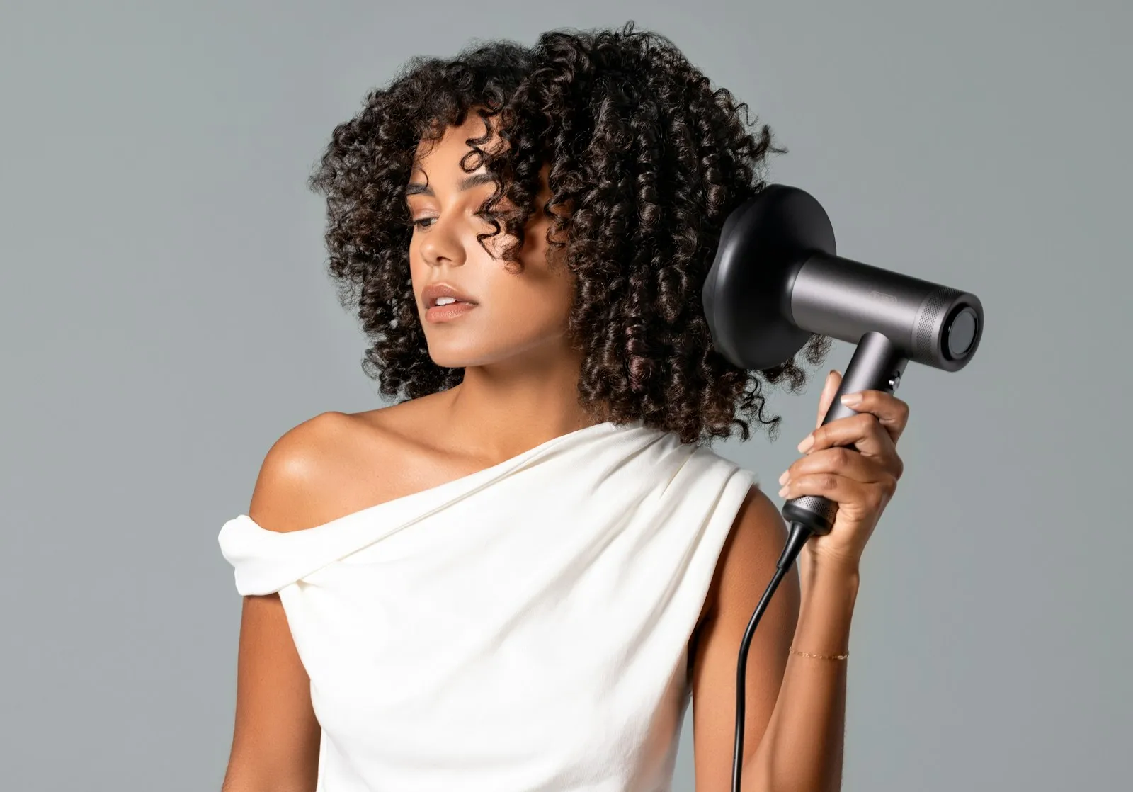 A woman with curly hair holds a TYMO hair dryer with a satisfied look on her face.
