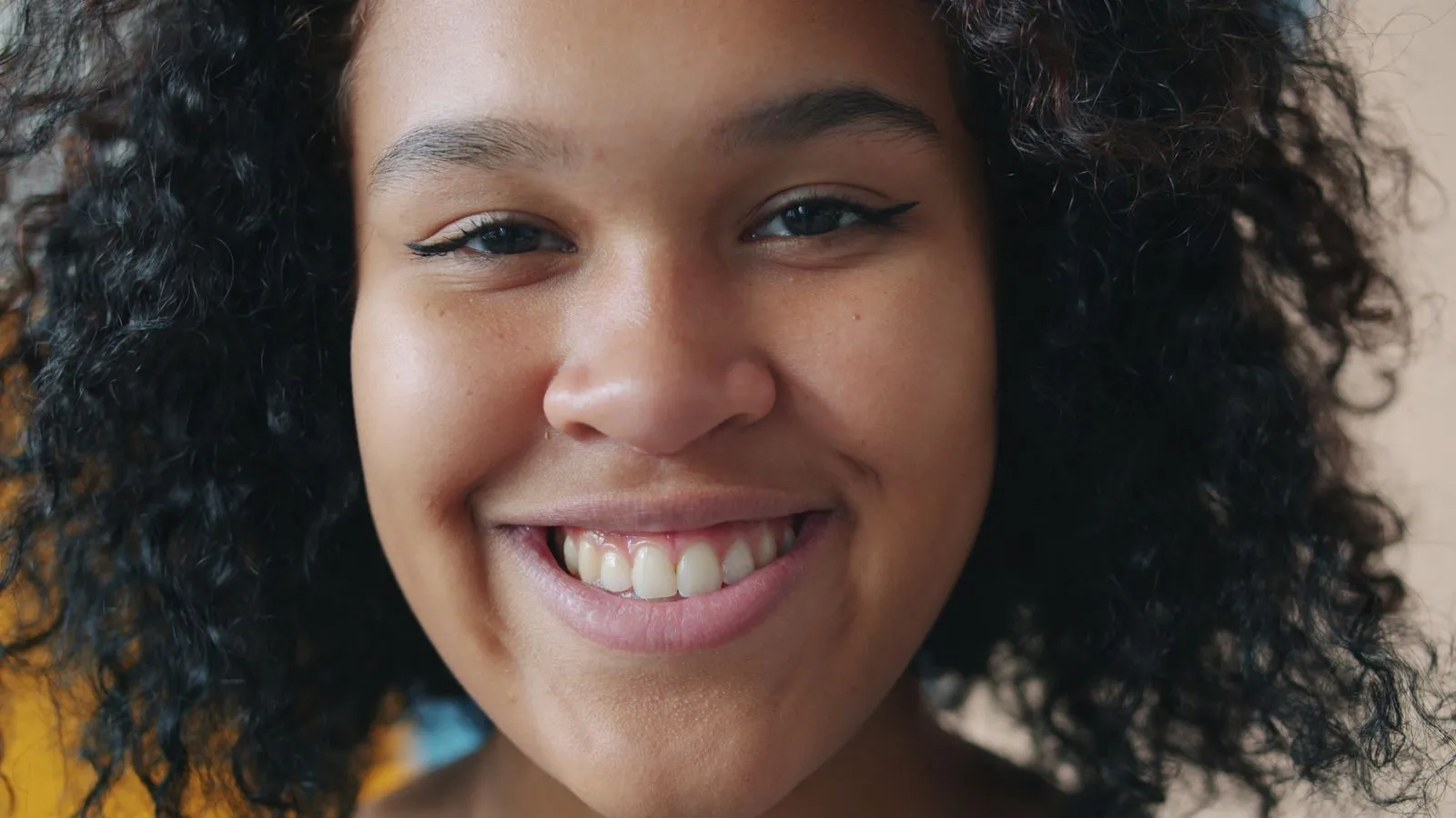 Close-up portrait of a young woman smiling with natural curly hair and bright expression.