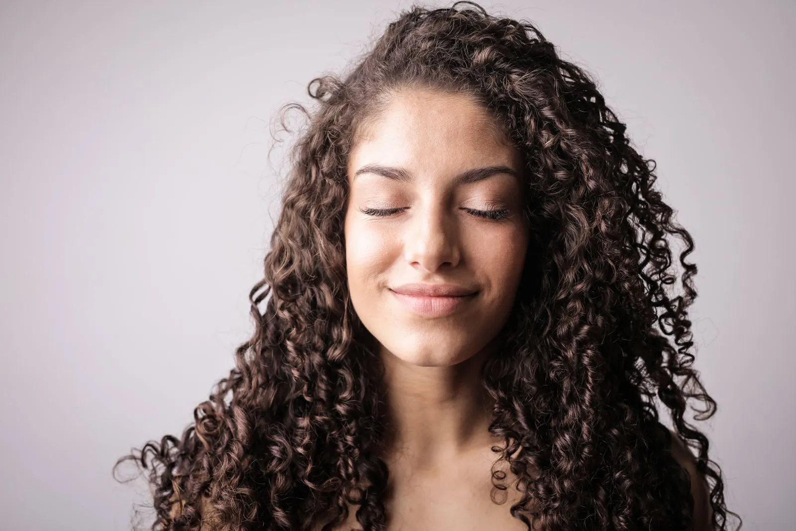 A close-up portrait of a smiling woman with curly hair, eyes closed, exuding happiness.