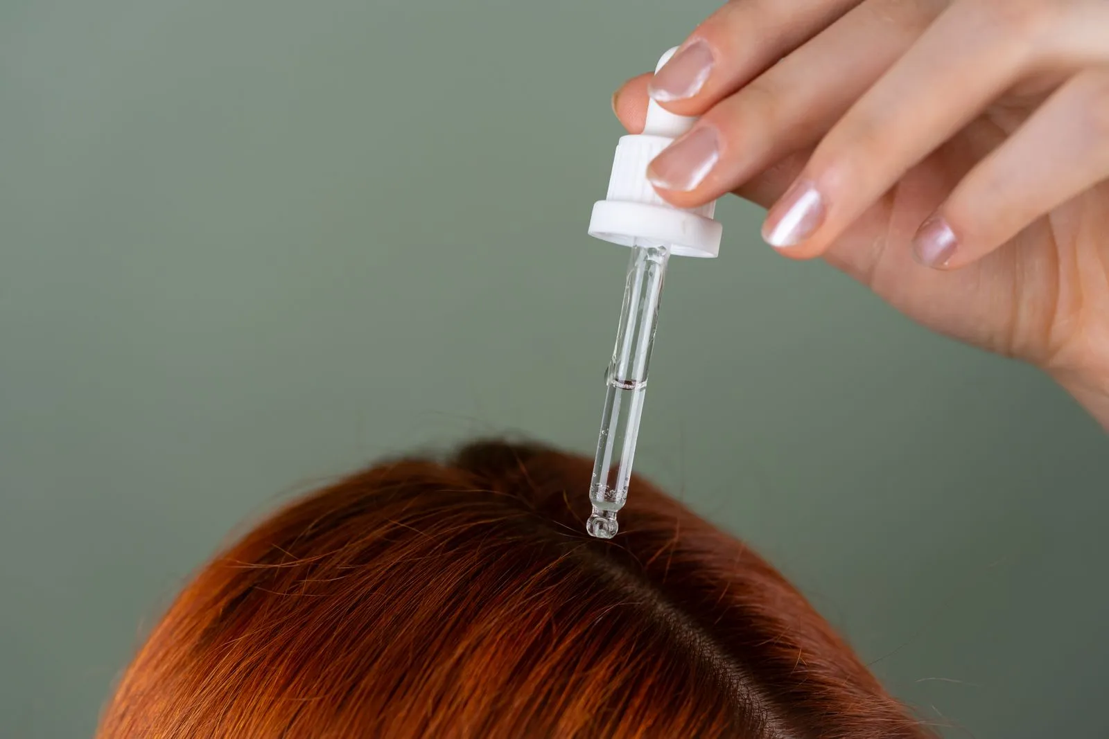 Close-up of applying serum to roots with a precision dropper on red hair