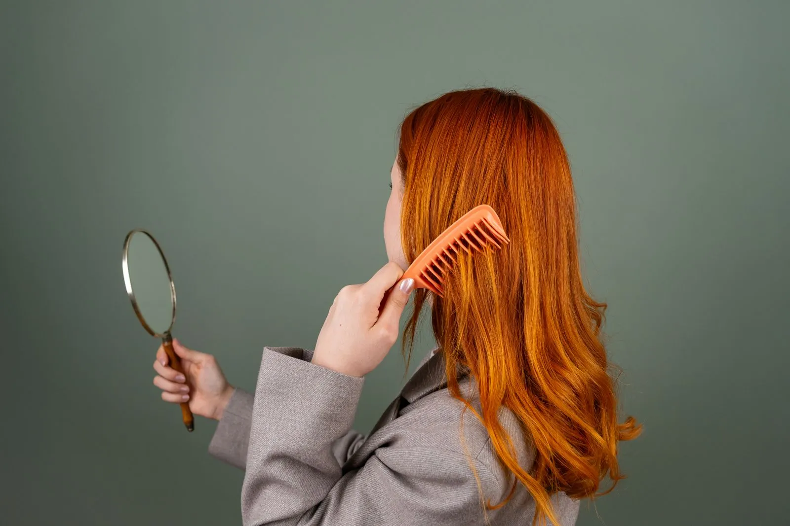 Red-haired woman using a comb while holding a mirror