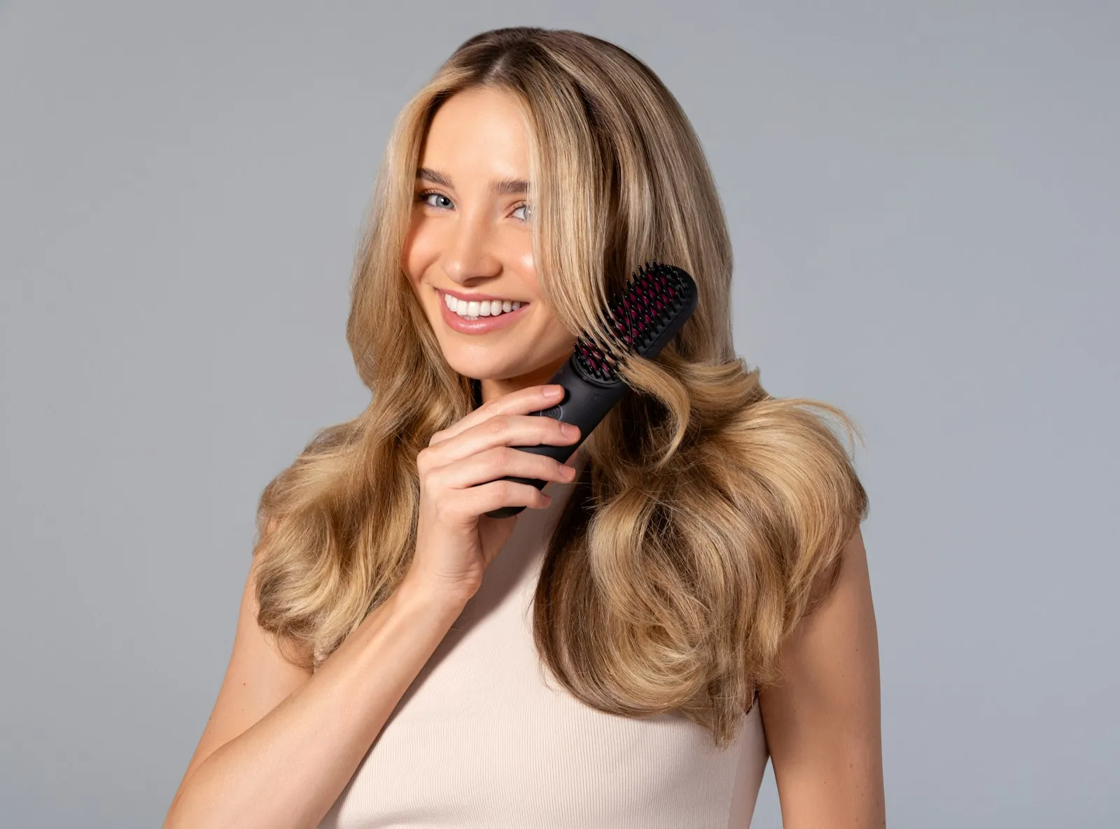 A woman with golden locks smiles as she gently brushes through her hair with a TYMO brush