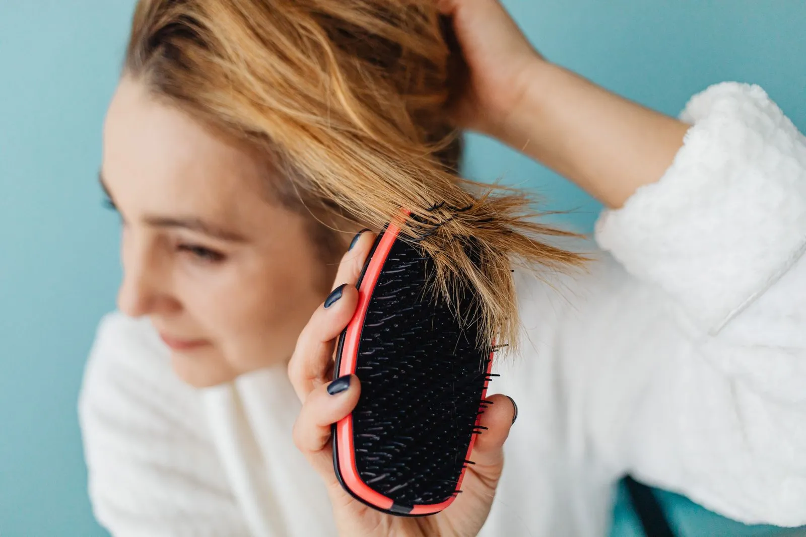 Close-up of a woman brushing her blonde hair with a red hairbrush indoors.