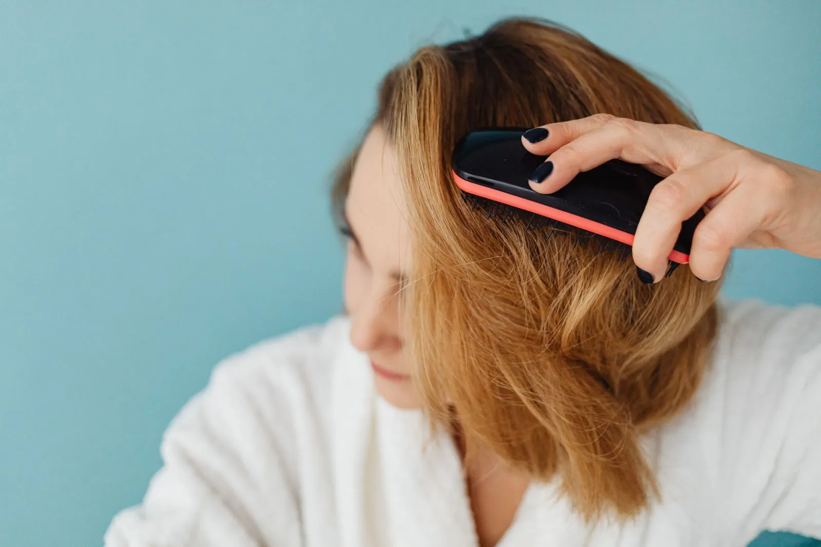 Close-up of a woman with brown hair brushing her hair in a bathrobe, representing a daily grooming routine.