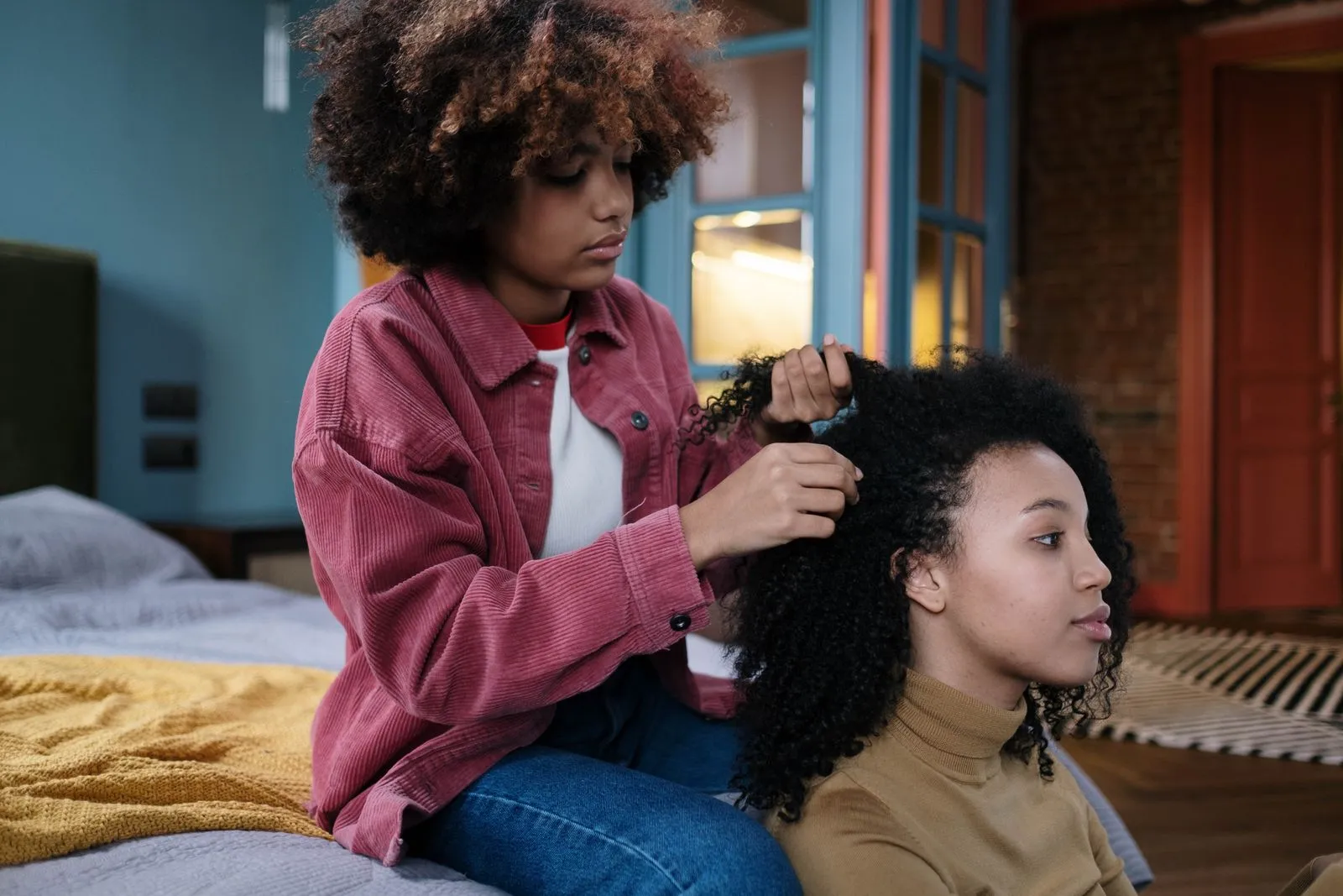 Two young women bonding as one styles the other's hair in a cozy room.