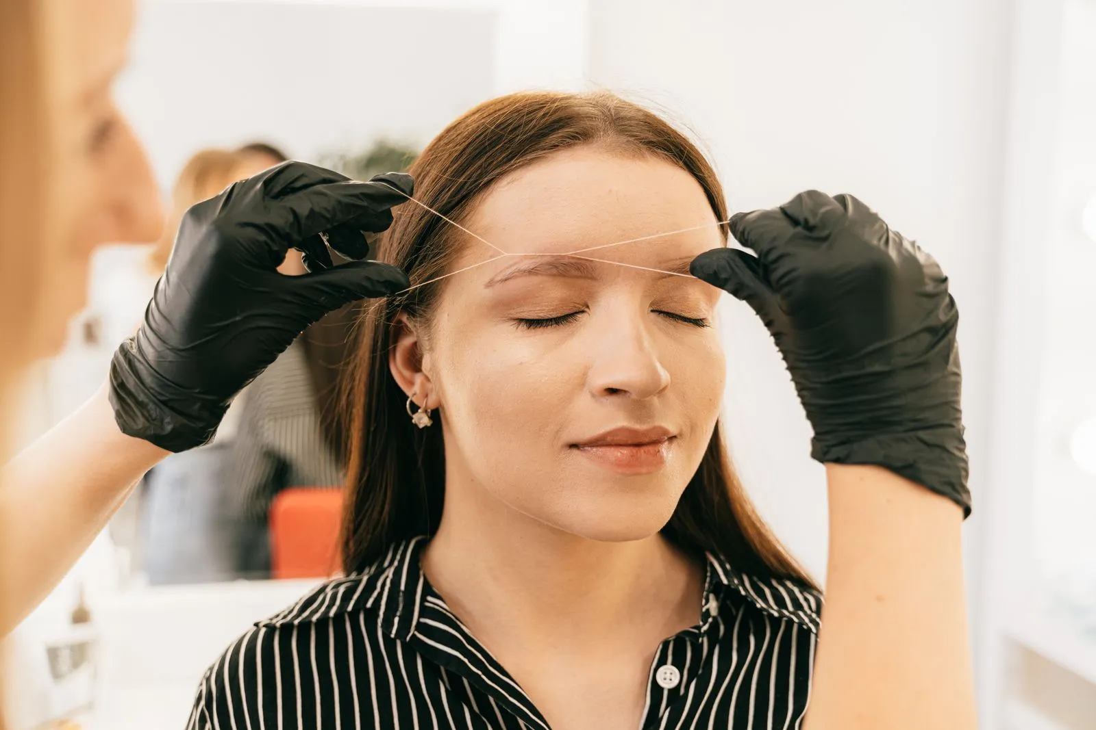 A woman receives precise eyebrow threading in a modern salon setting.