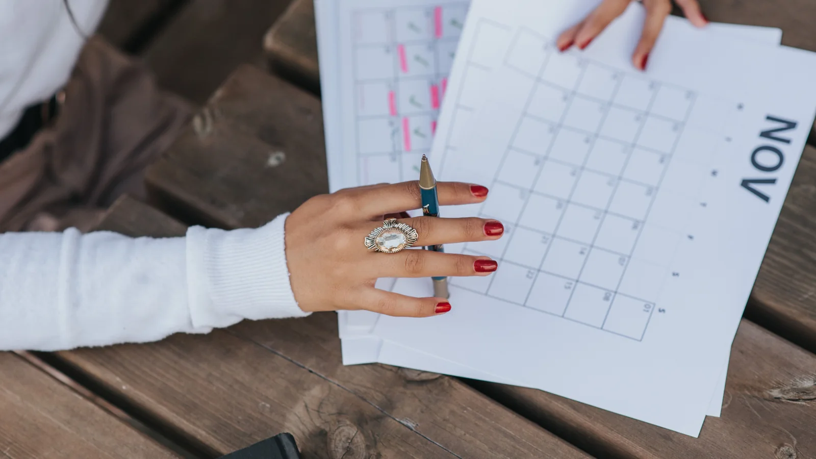 Hands writing in a monthly planner on a wooden table.