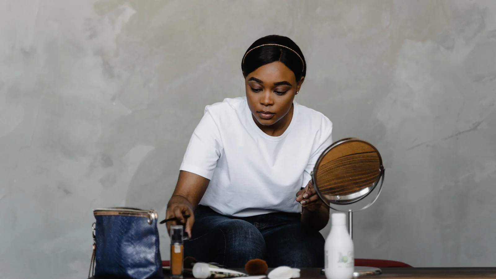 A person sitting at a table with a mirror, cosmetics and make-up brushes.