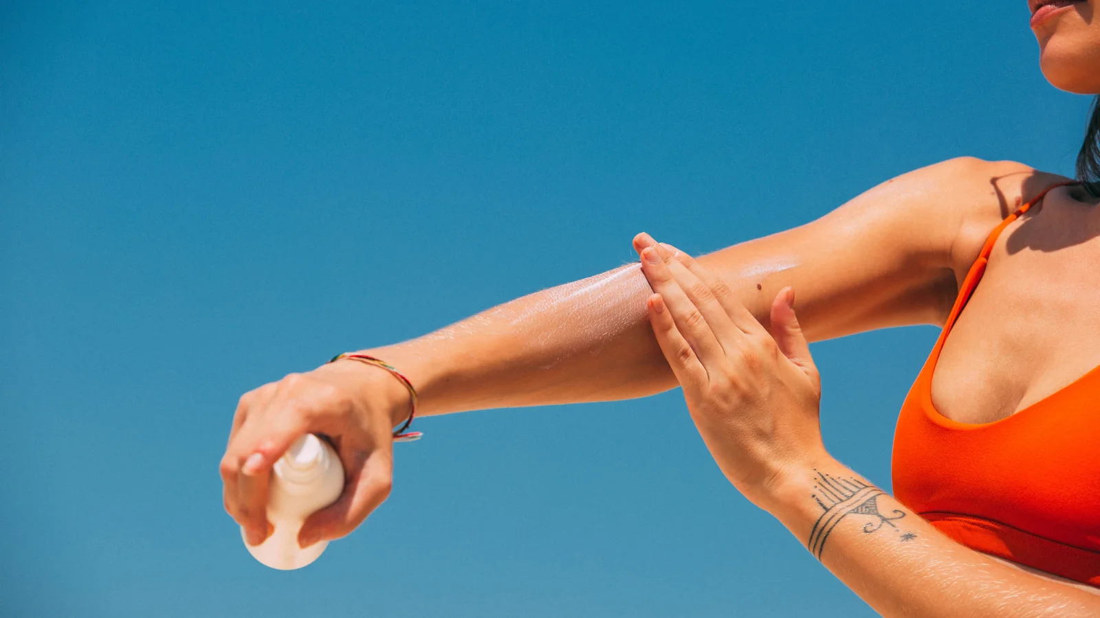 A person spreading a light-coloured lotion on their forearm outdoors.