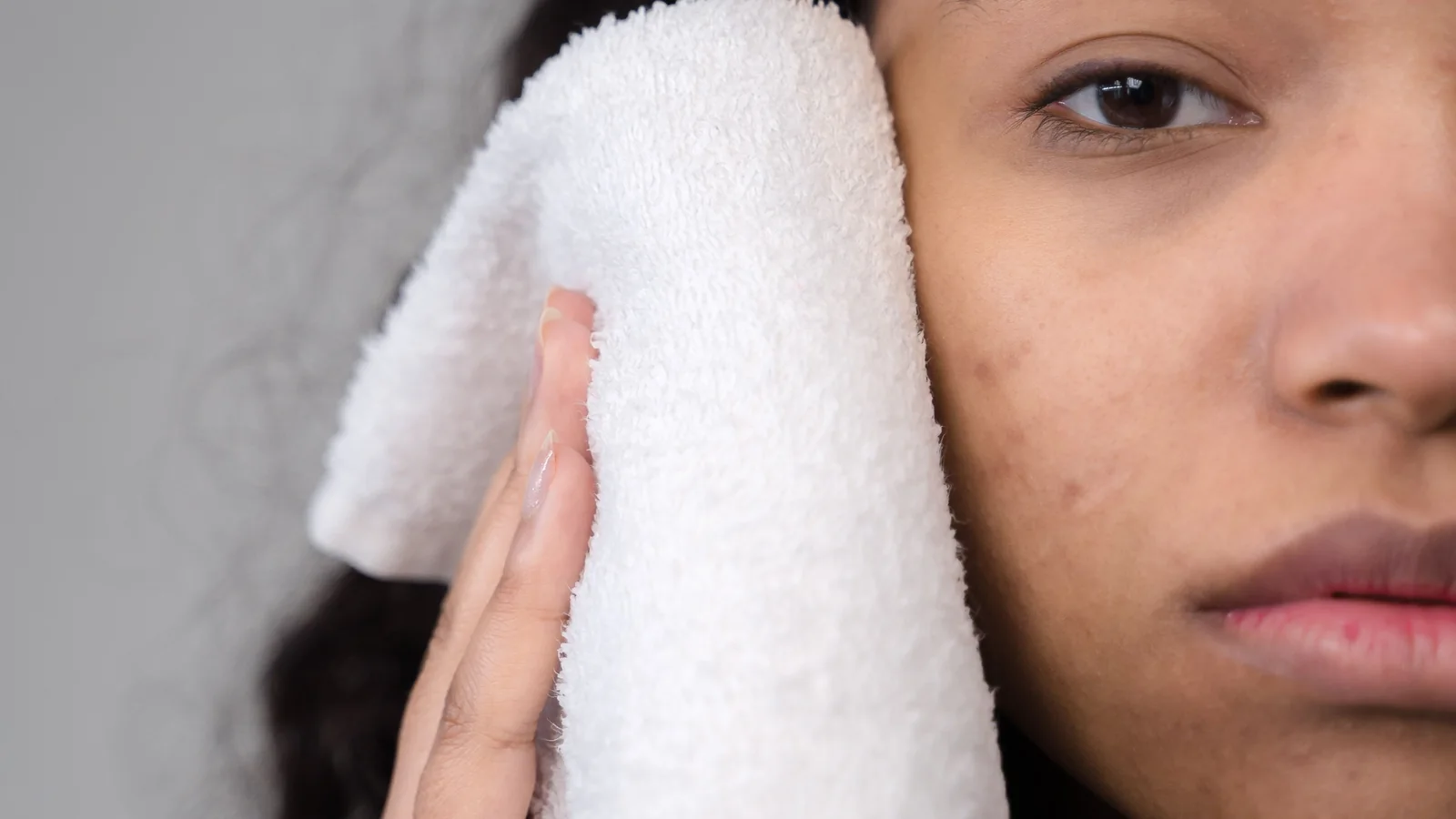 A person holding a white face towel against their cheek.
