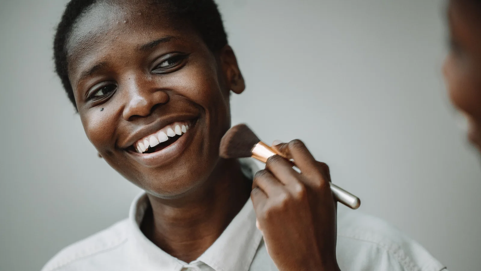 A smiling woman touching a make-up brush to her cheek.