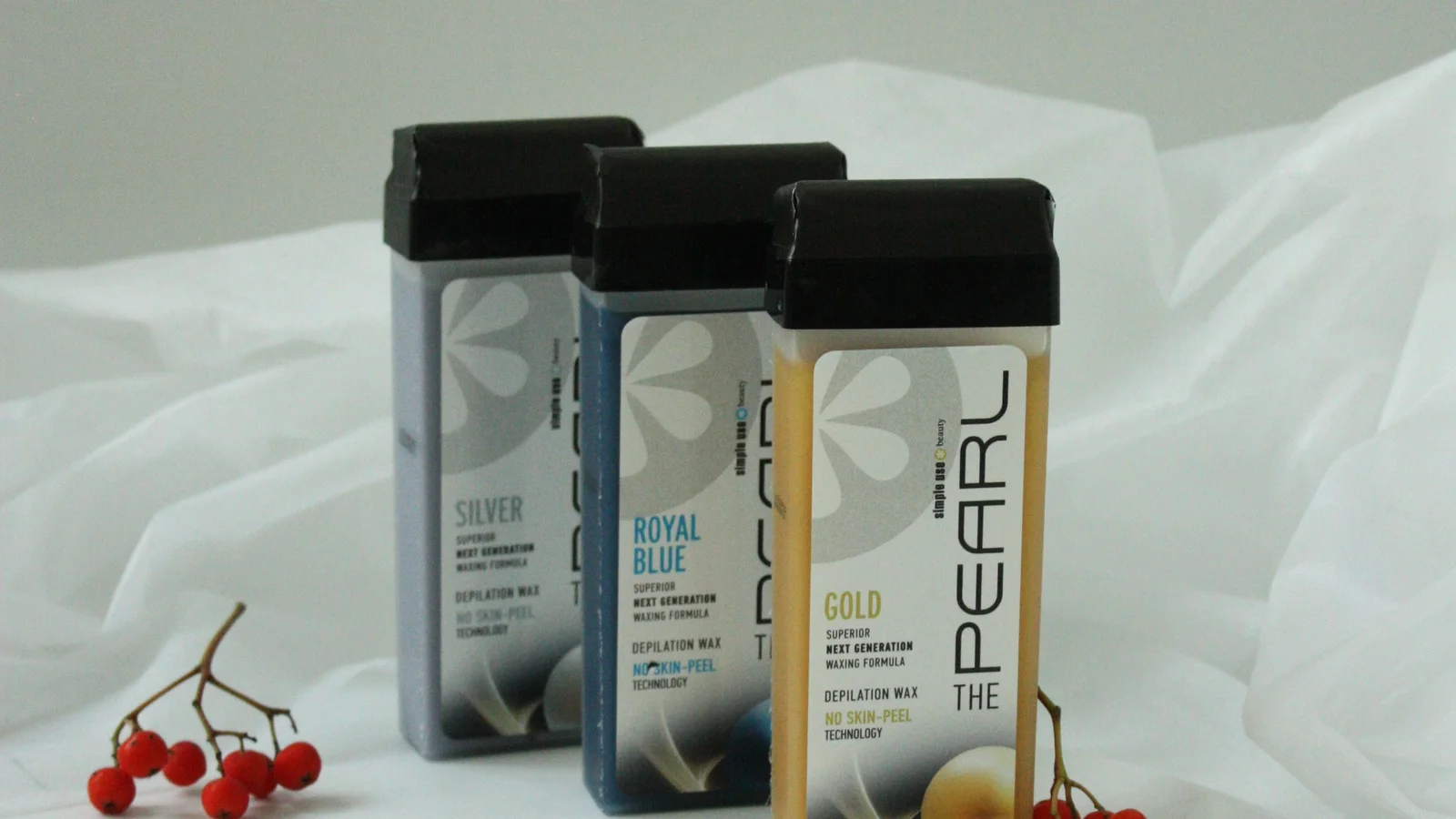 Three roll-on wax cartridges on pale fabric beside small red berries.