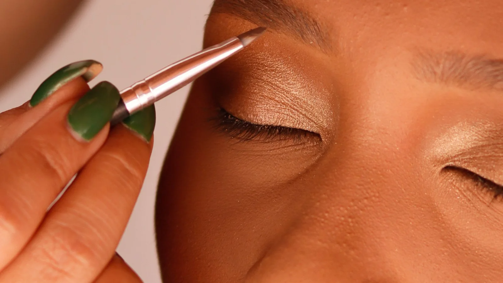 A make-up artist working beside a woman's upper eyelashes with a small tool.
