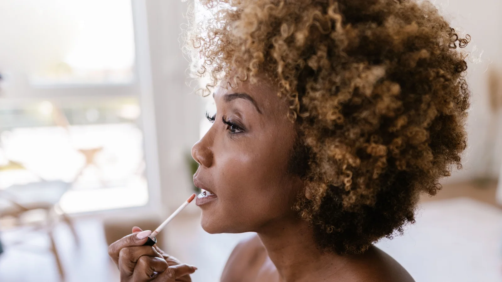 A woman applying lip gloss while looking into a mirror.