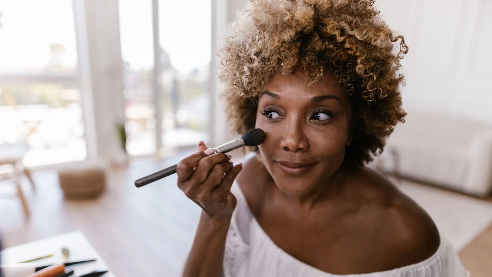 A woman applying make-up to her cheek with a rounded brush.