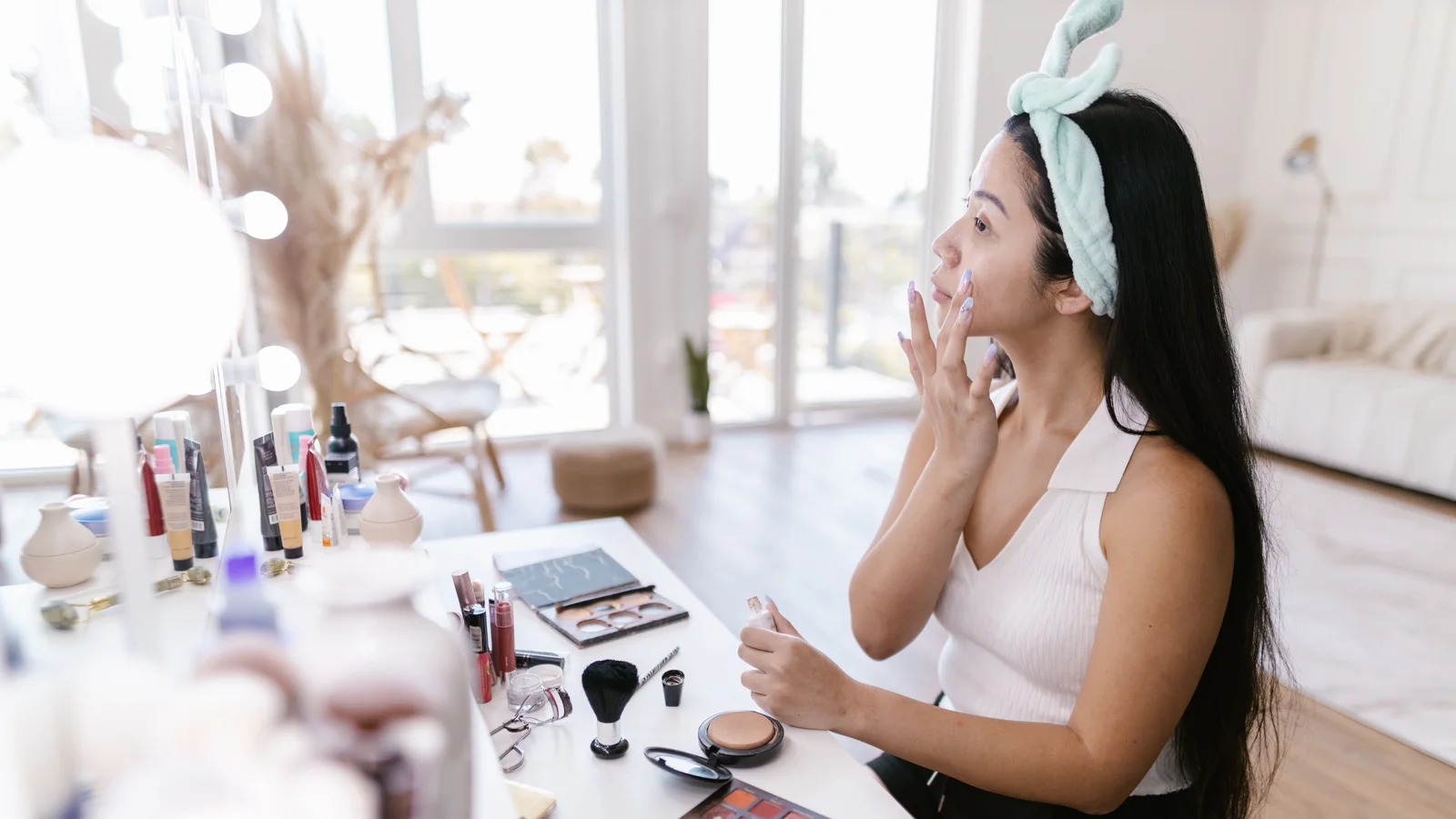 A woman pressing a make-up sponge to her cheek at a dressing table.